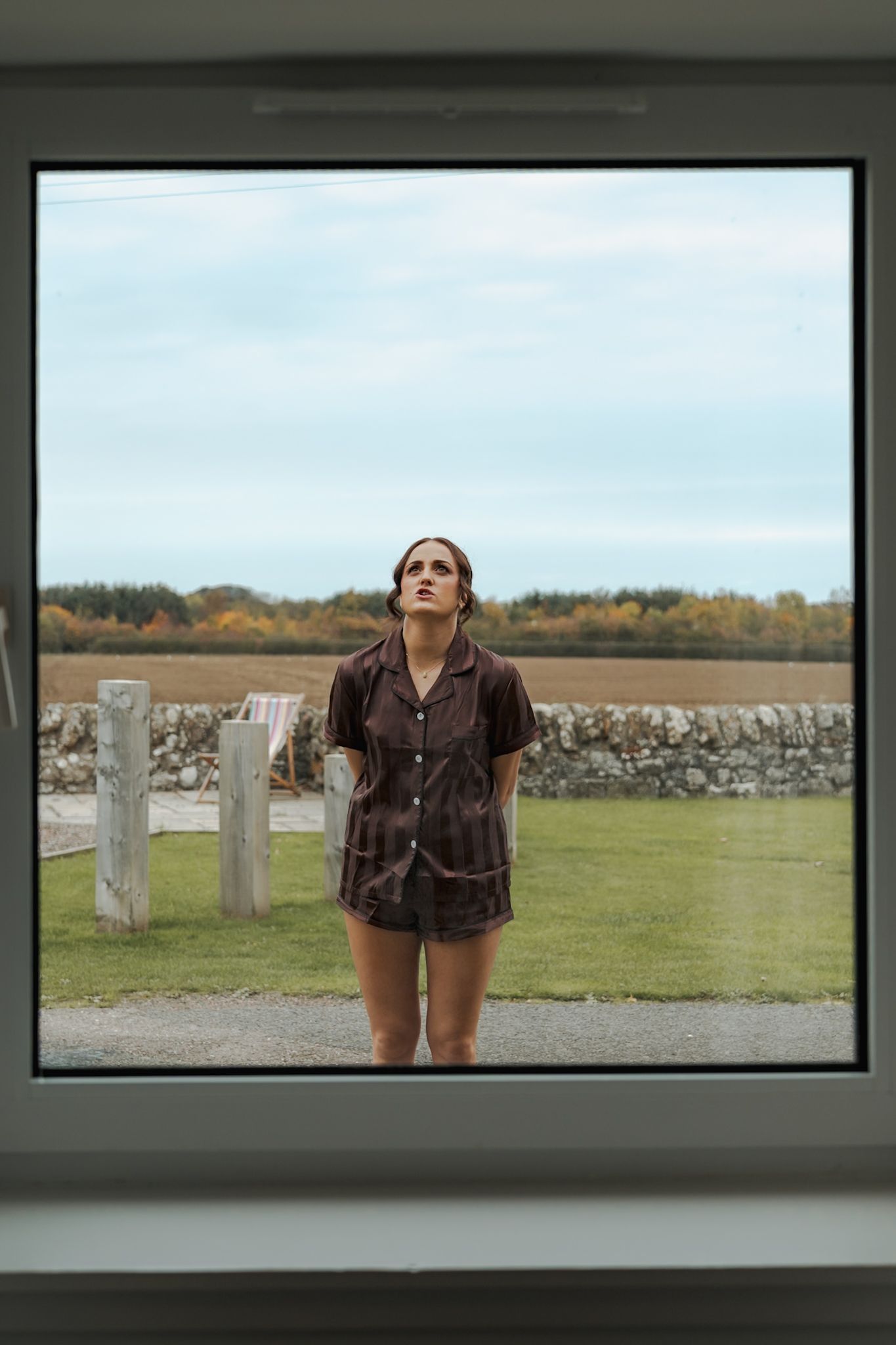 A person in a brown shirt stands in a field with autumn trees and stone walls visible in the background.