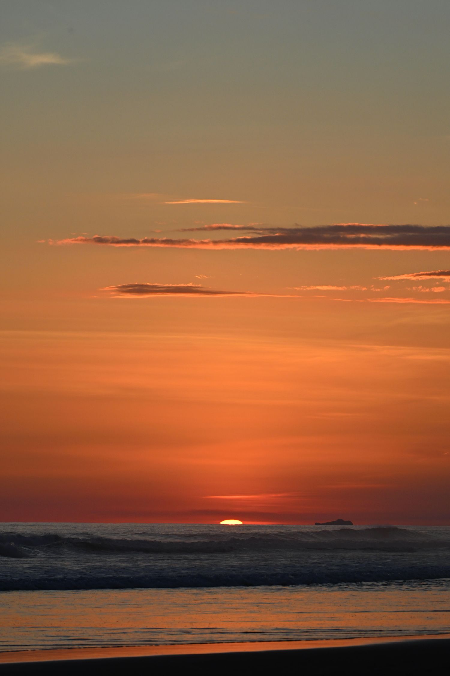 Vibrant orange and red sunset over ocean waves with sun setting on horizon and scattered clouds in warm sky.