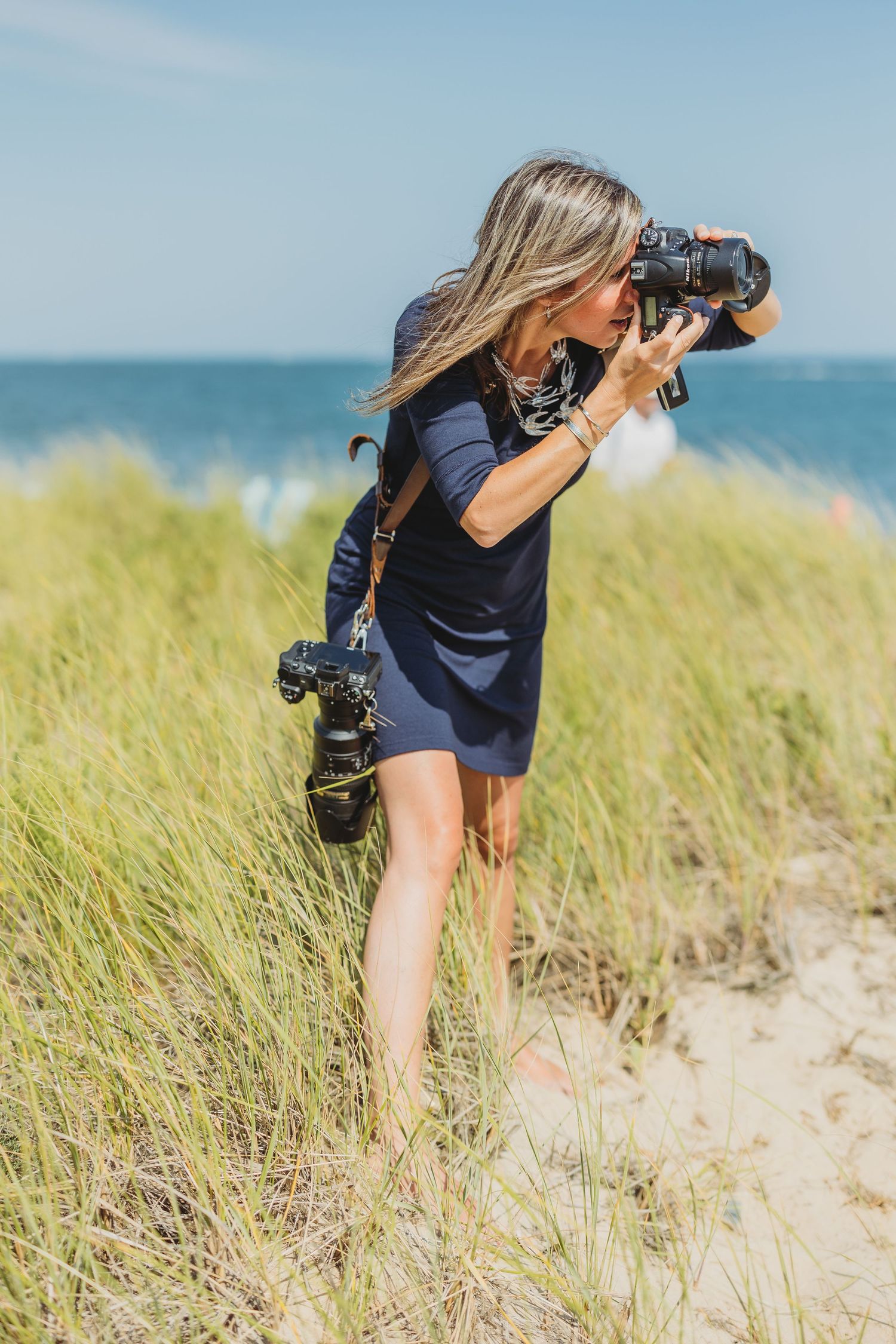 Photographer with camera equipment crouching in beach grass along the coastline.