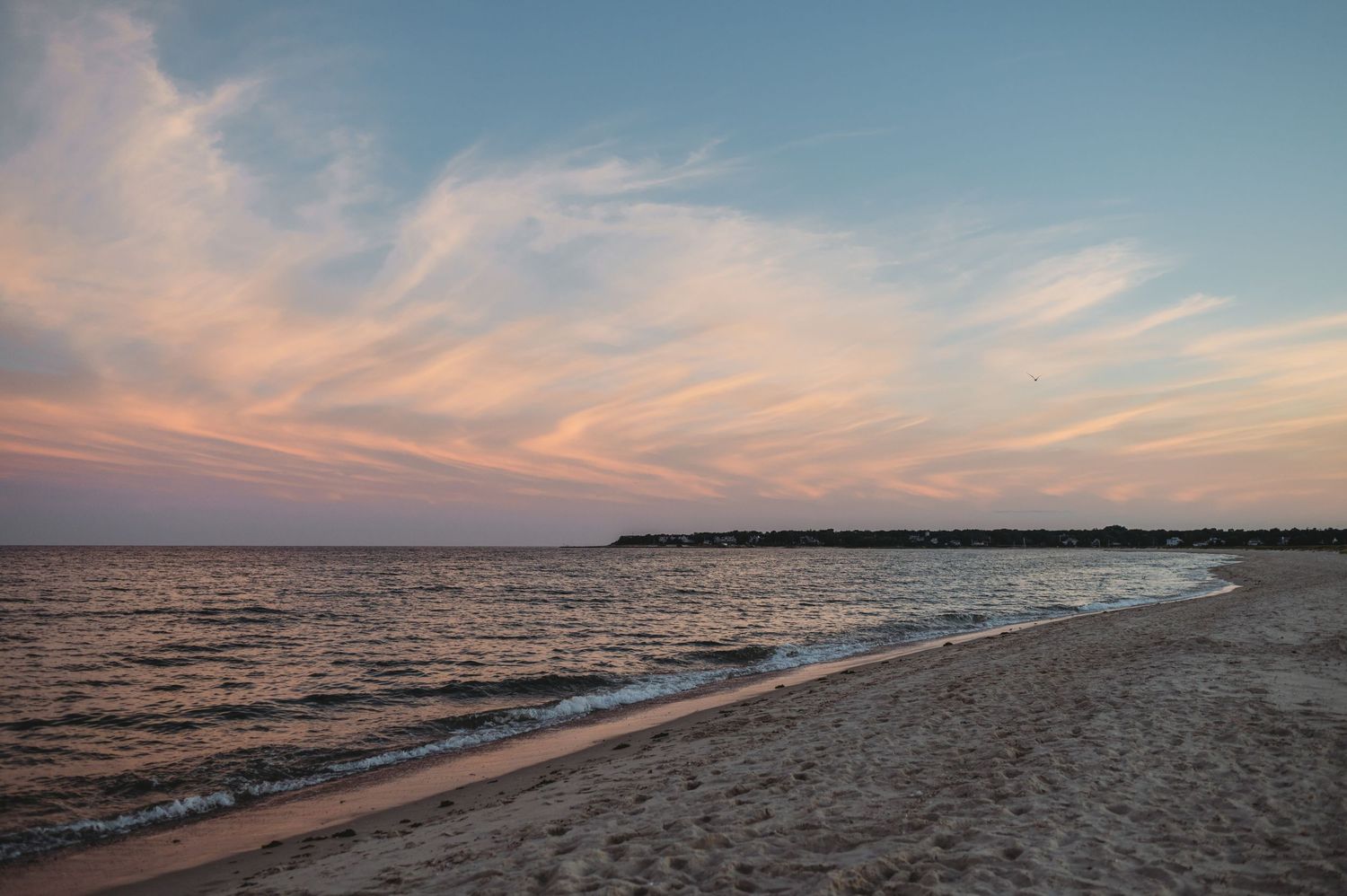 Peaceful beach sunset with pink clouds reflecting over calm waters and sandy shore.