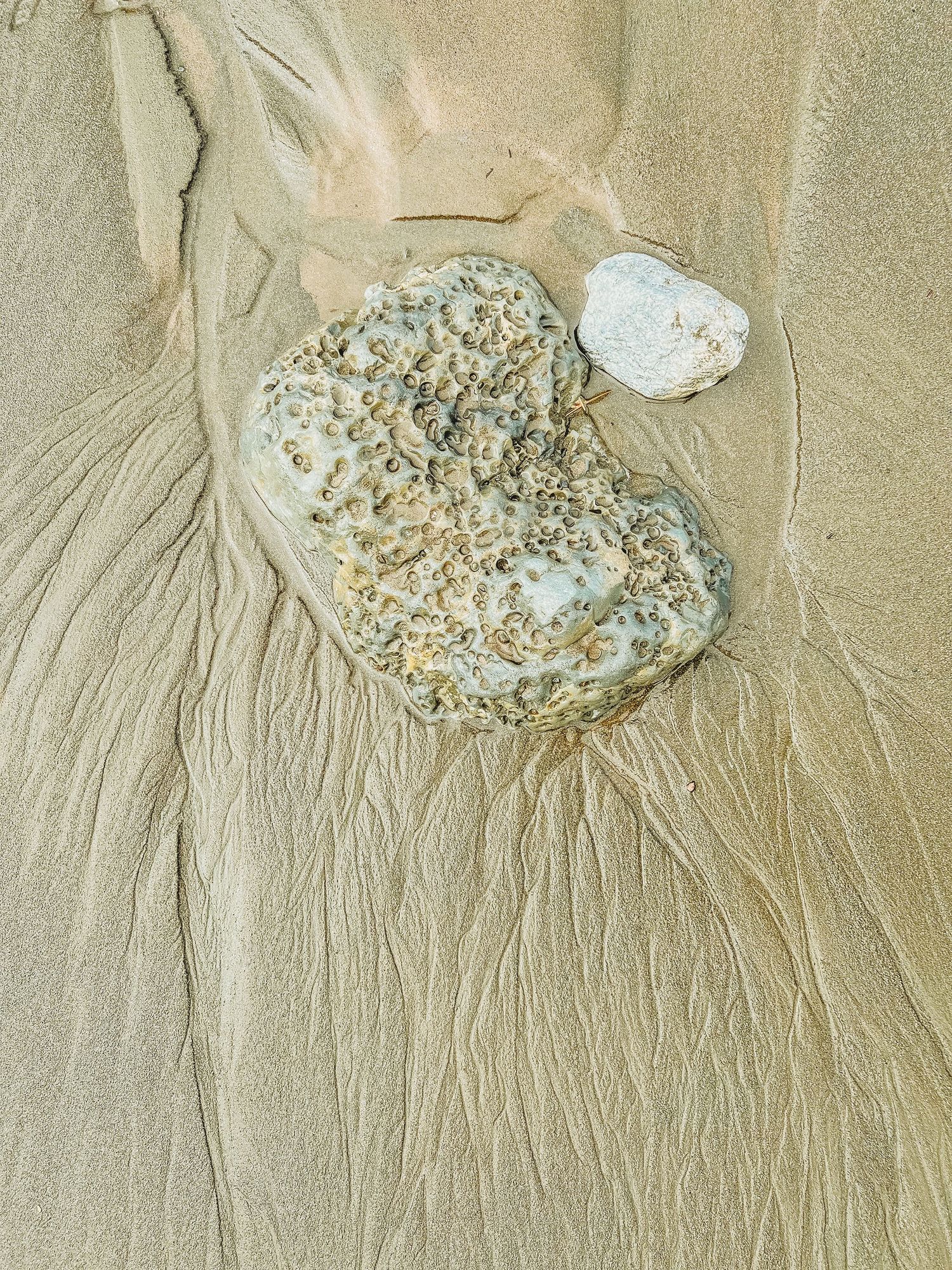 Textured patterns in sand around a weathered stone on a beach.