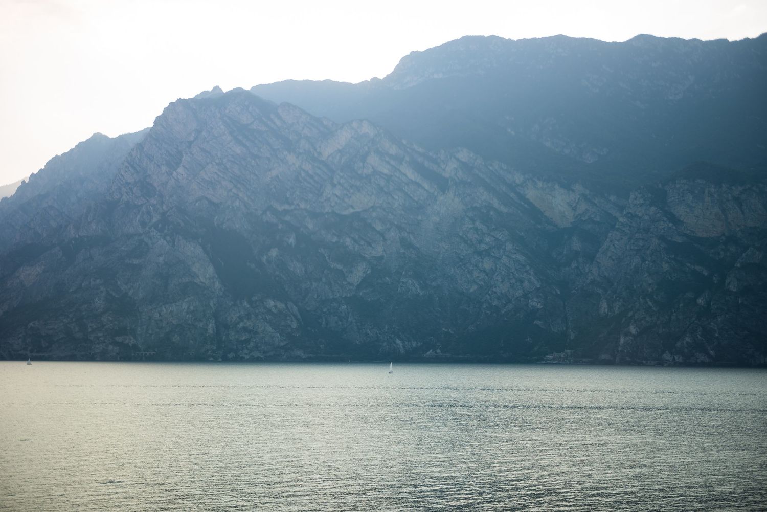 Dramatic mountain range rising above a serene lake with misty atmosphere.