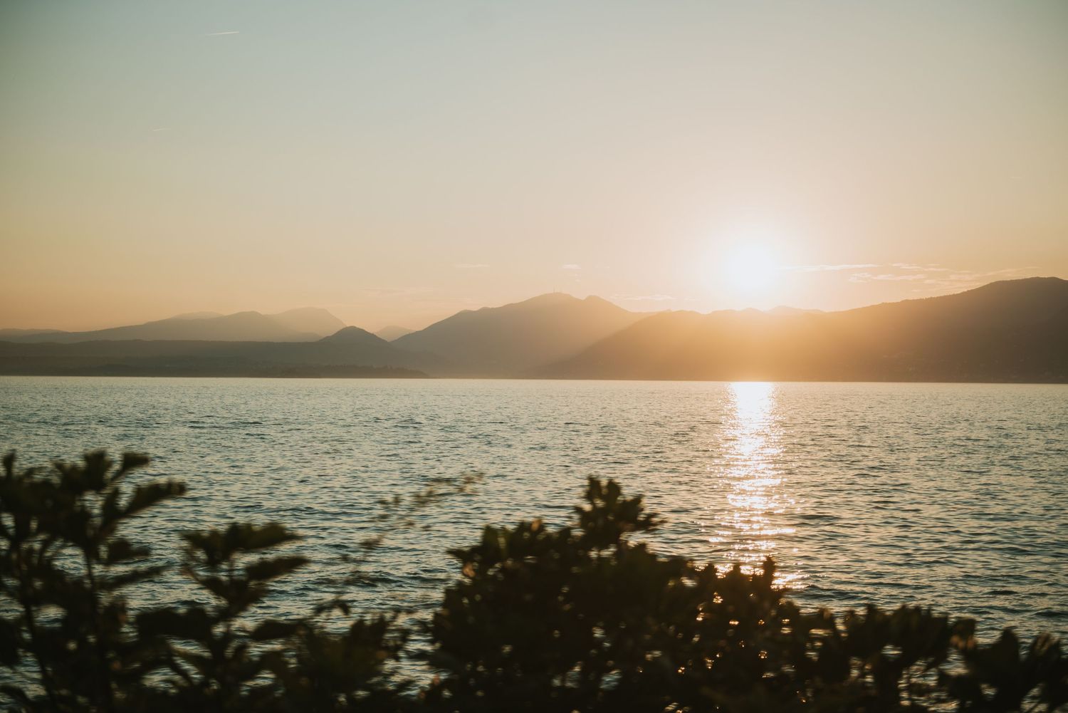 Golden sunset over a lake with mountains creating a silhouette against the sky.