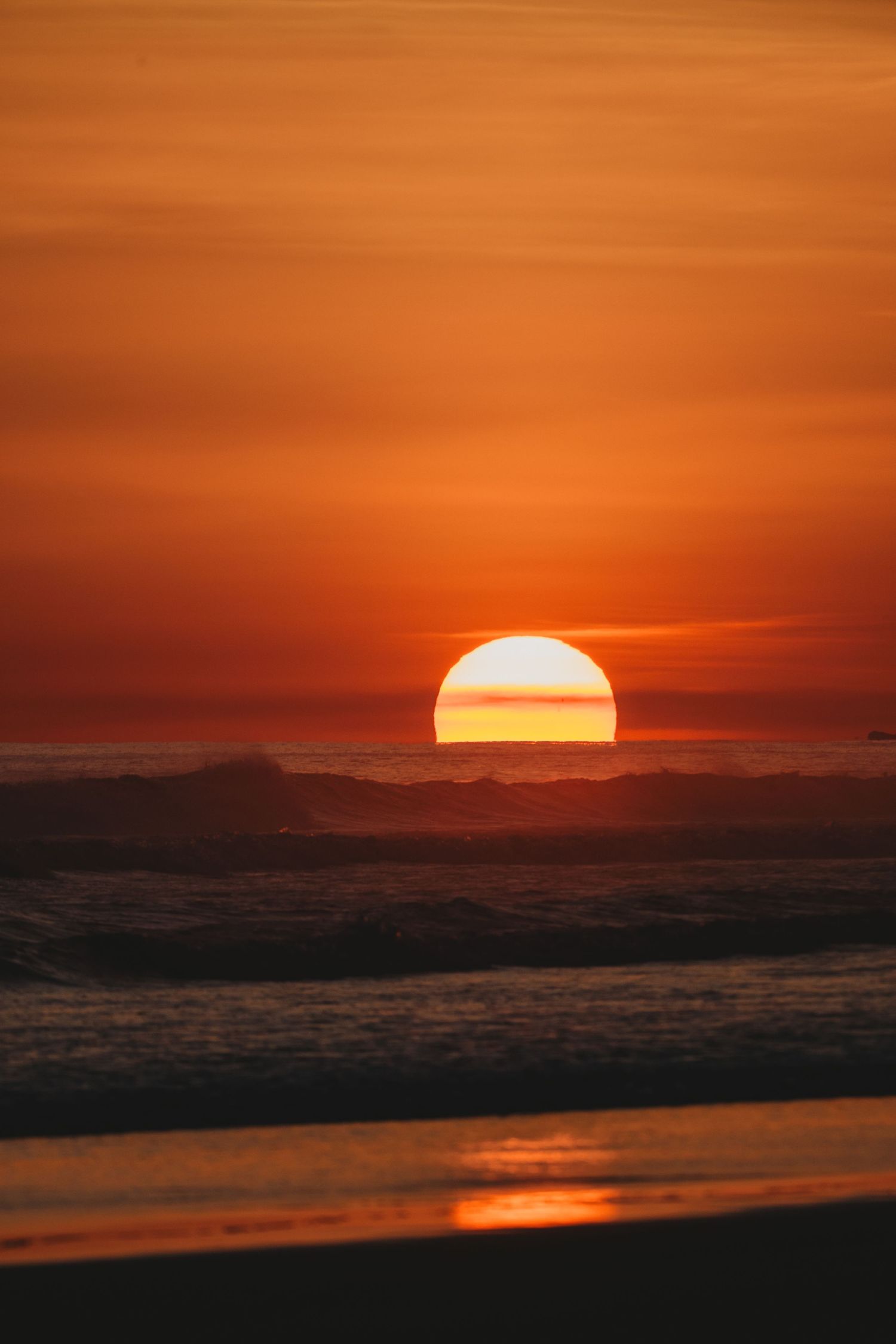 A stunning ocean sunset with a large glowing sun touching the horizon, casting deep orange and red hues across the sky and sea.