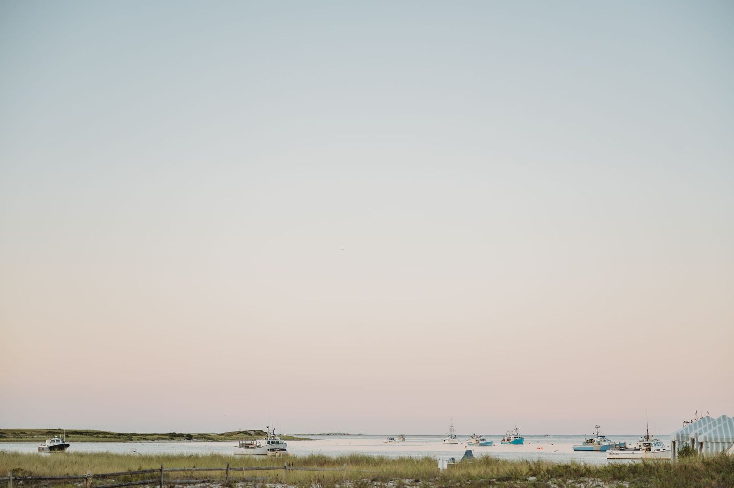 Panoramic view of a serene harbor with boats dotting the horizon at sunset.