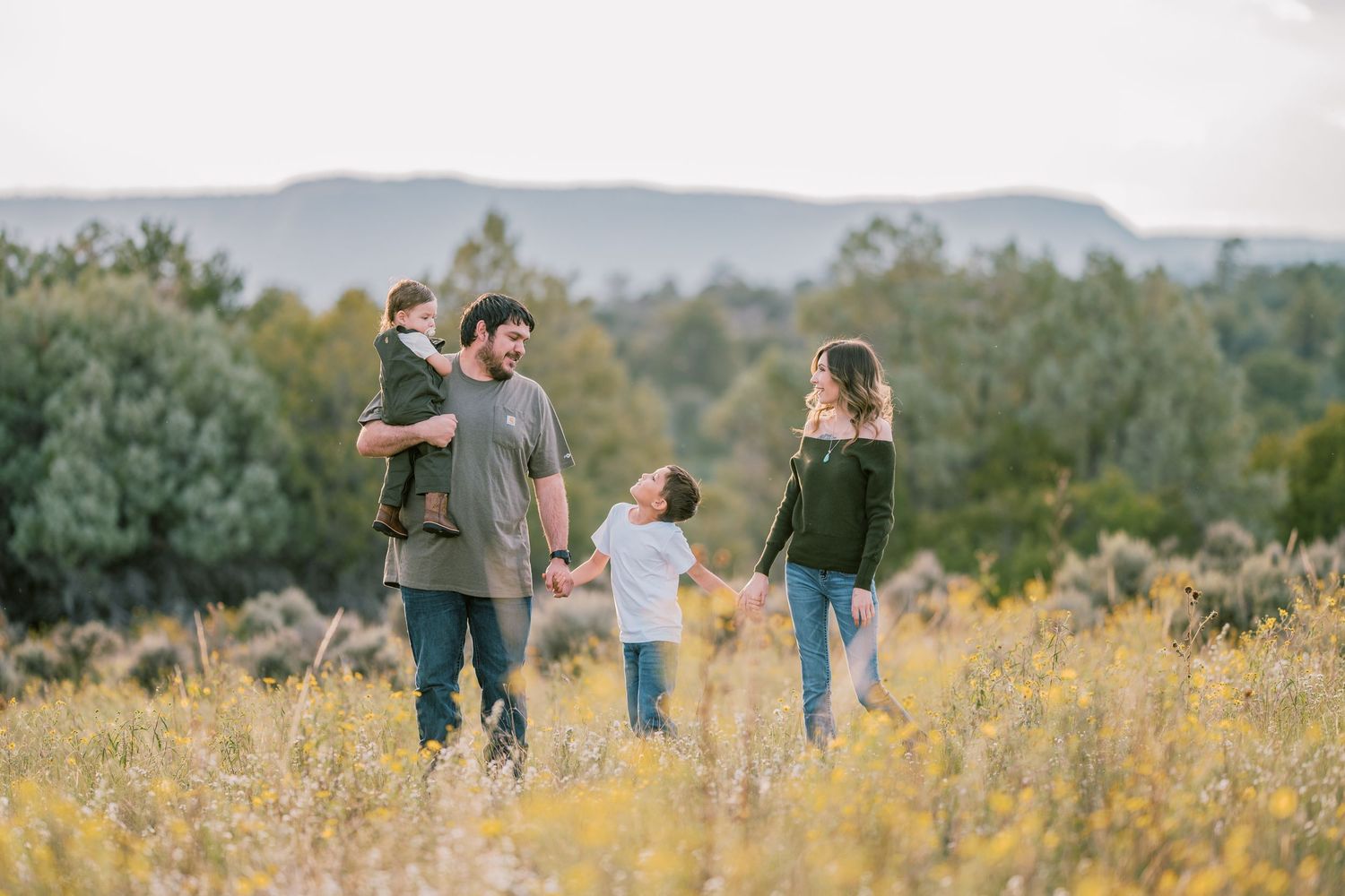 Family walking through tall yellow wildflowers with mountain landscape behind them.