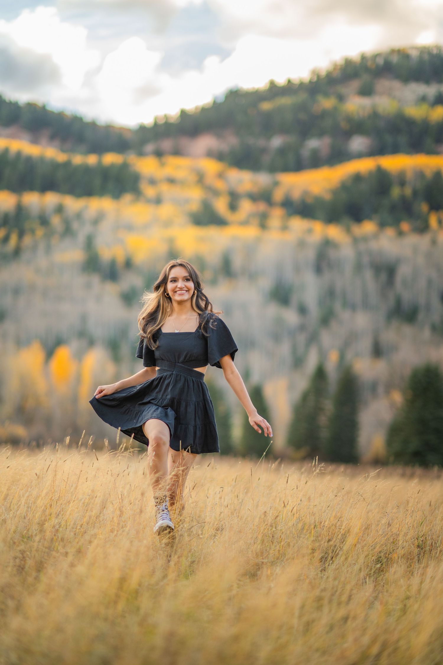 A person in a black dress twirls through a golden autumn meadow with aspen-covered mountains in the background.
