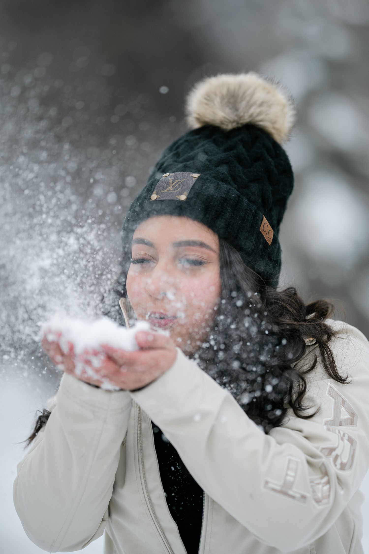 Person in a white winter coat and black beanie blowing snow from their hands in a playful sequence.