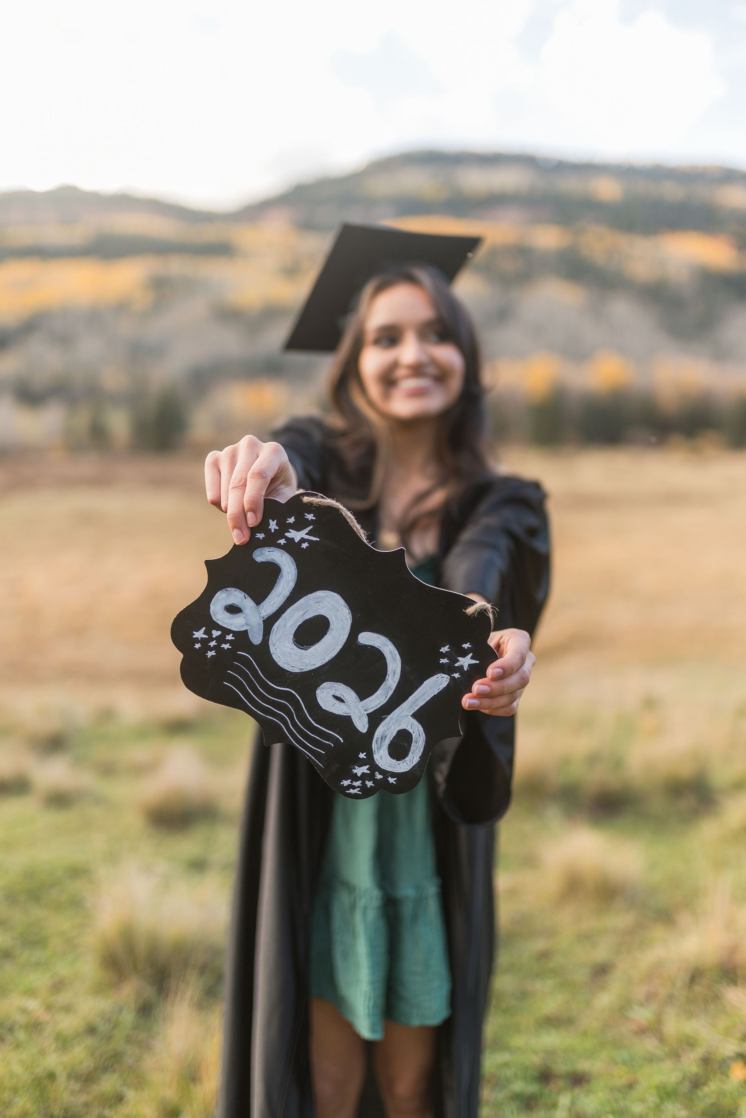 Person holds up handmade milestone signs showing baby footprint growth against a scenic mountain landscape background.