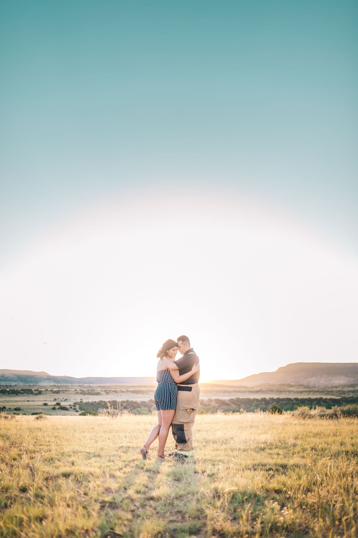 A couple embraces in a vast field during a golden sunset.