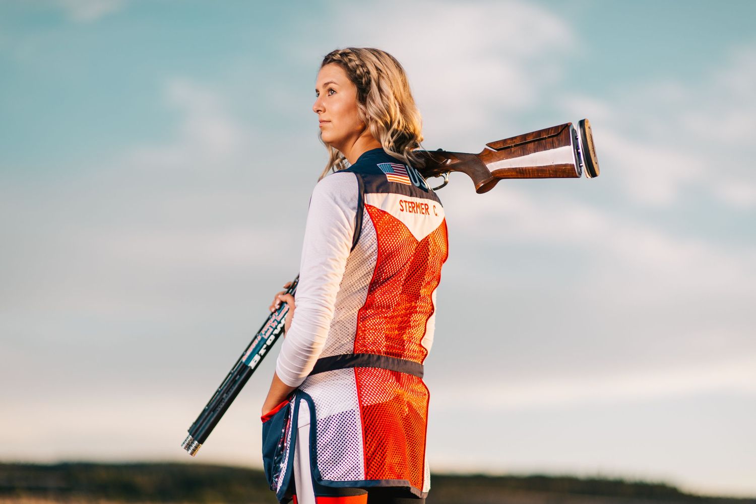 Sport shooter practicing with competition gear against sunset sky.