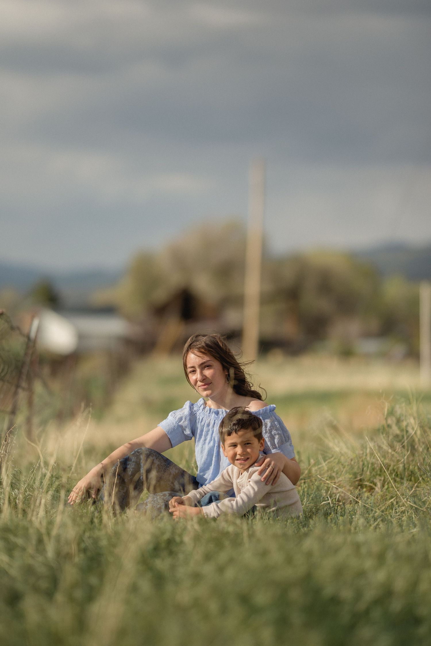 Two people lay together in a sunny meadow of tall grass on a cloudy afternoon.
