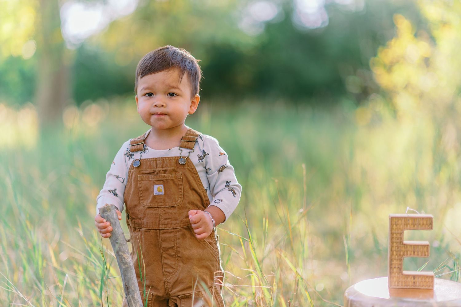 A child wearing brown overalls plays in a sunny meadow during golden hour.