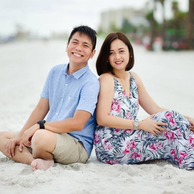A couple relaxes together on a white sandy beach wearing coordinated summer outfits.