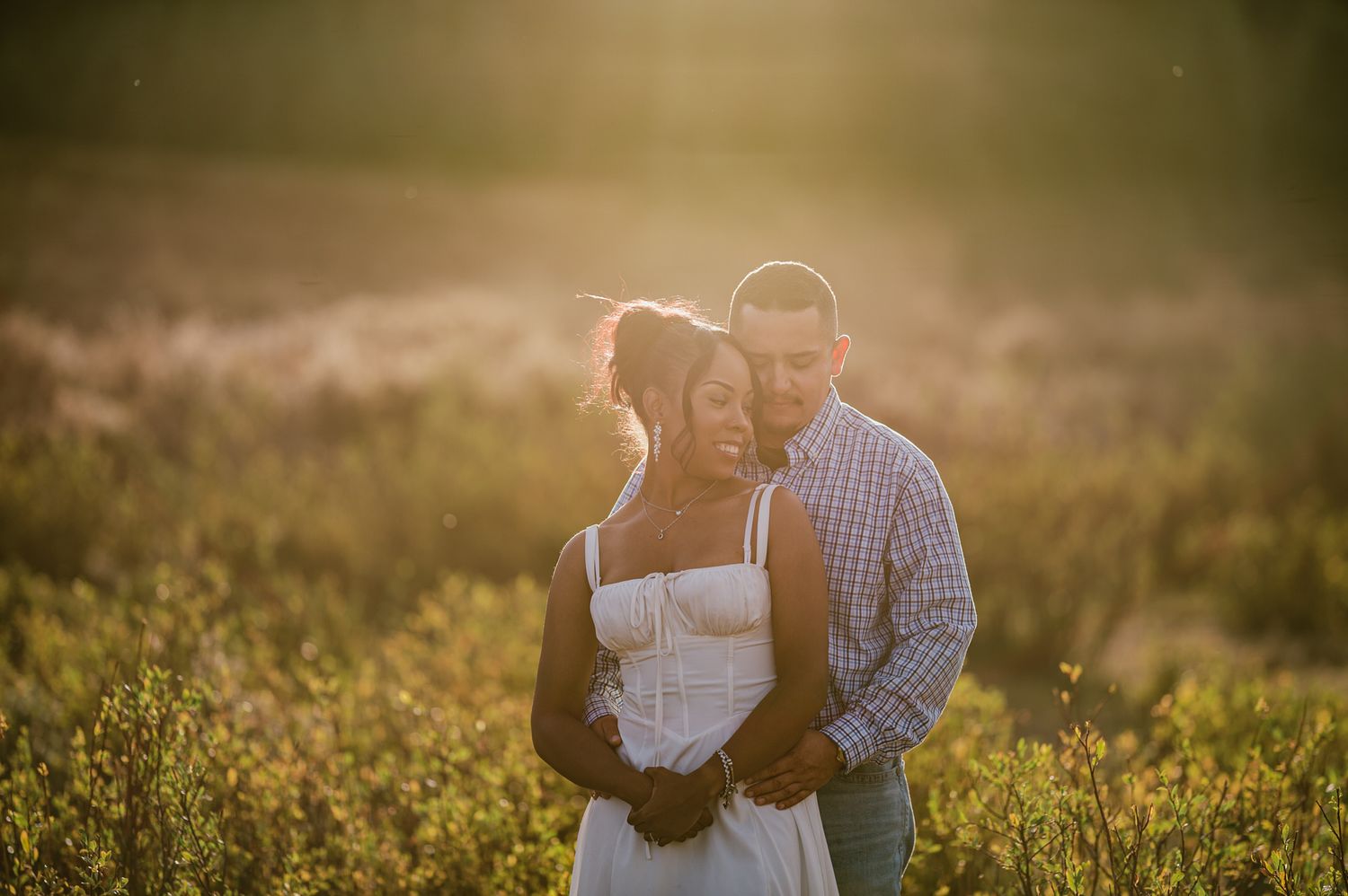 Couple embracing in golden sunset light in a wildflower field, romantic engagement photo outdoors.