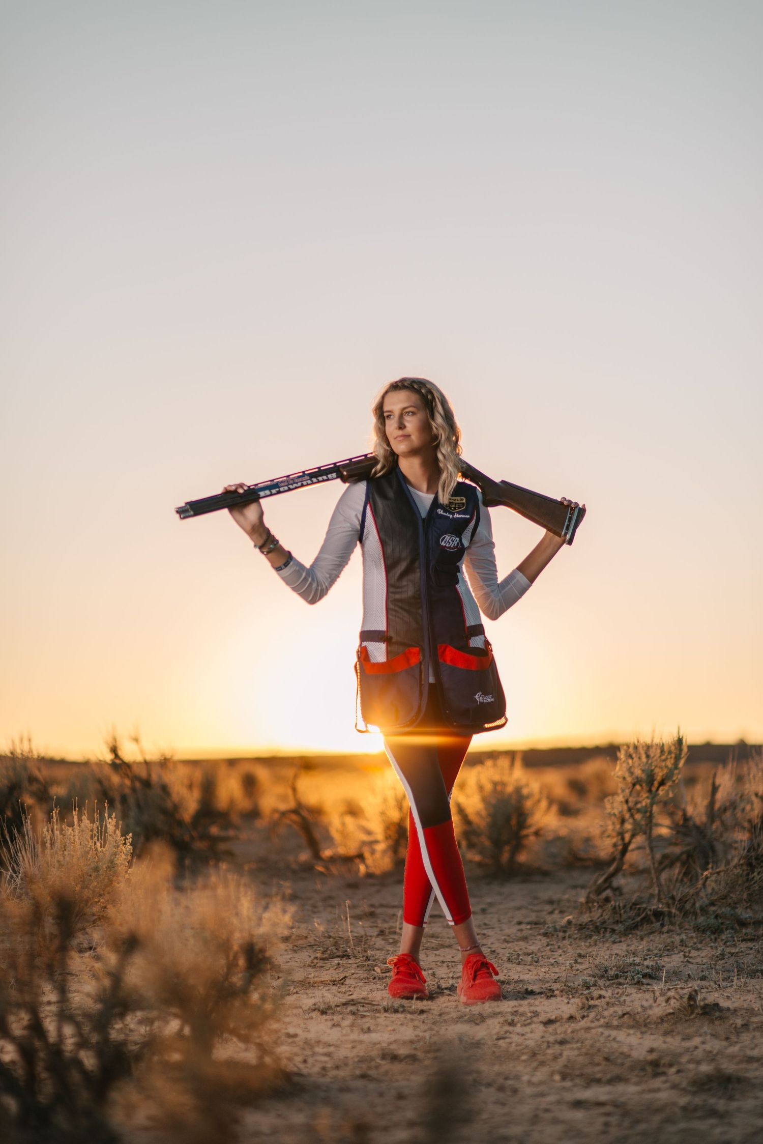 Silhouetted figure poses with flowing dress in dramatic desert sunset landscape.