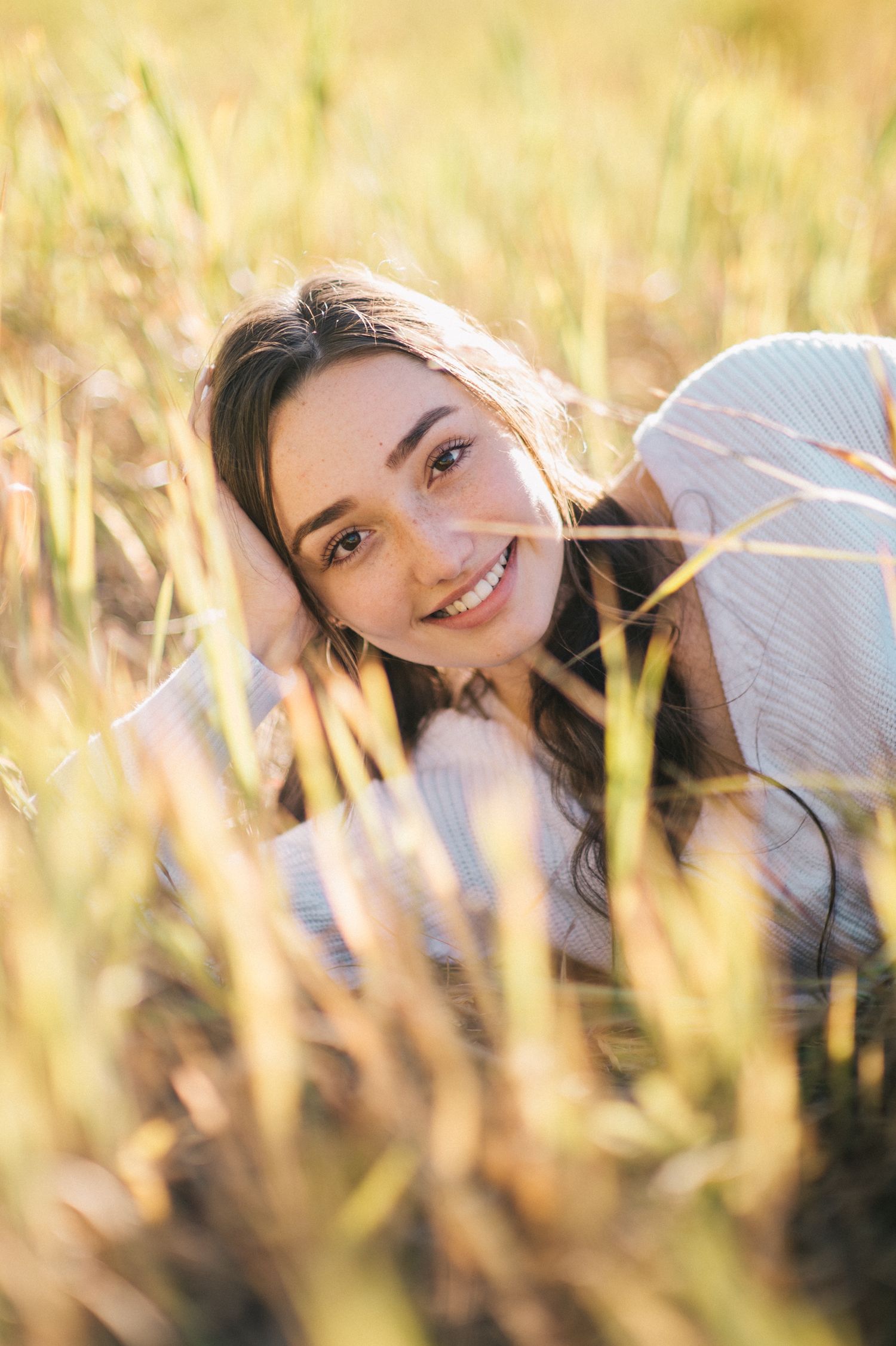 Sun-drenched portrait through tall grass creating dreamy natural lighting effect.