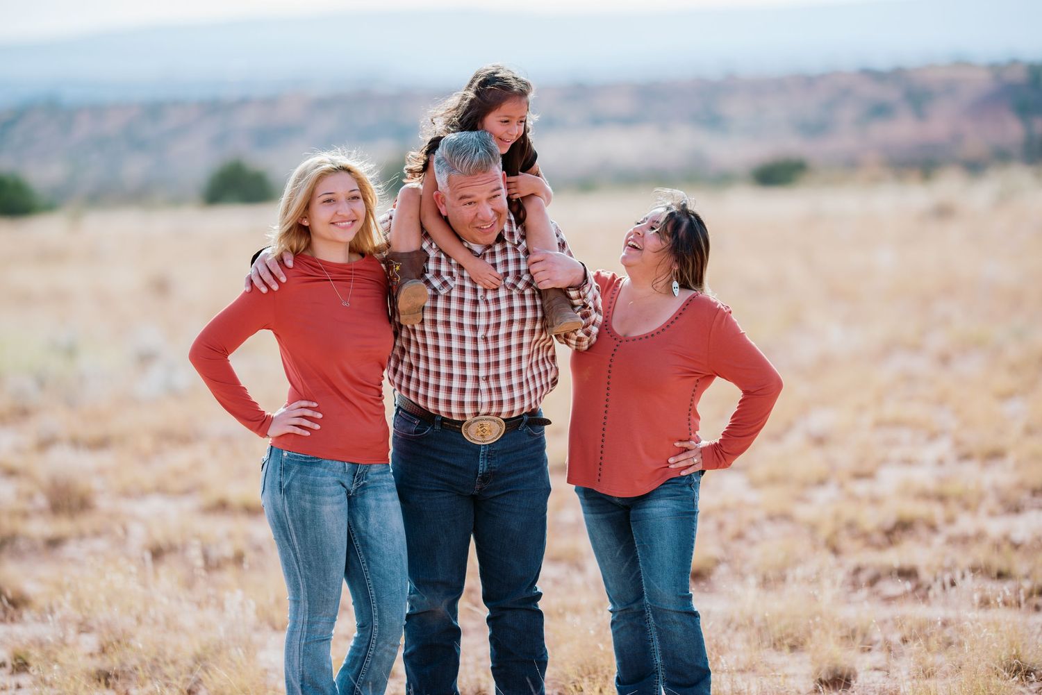 A cheerful group in coordinating casual outfits laughs together while standing in a sunlit desert landscape.