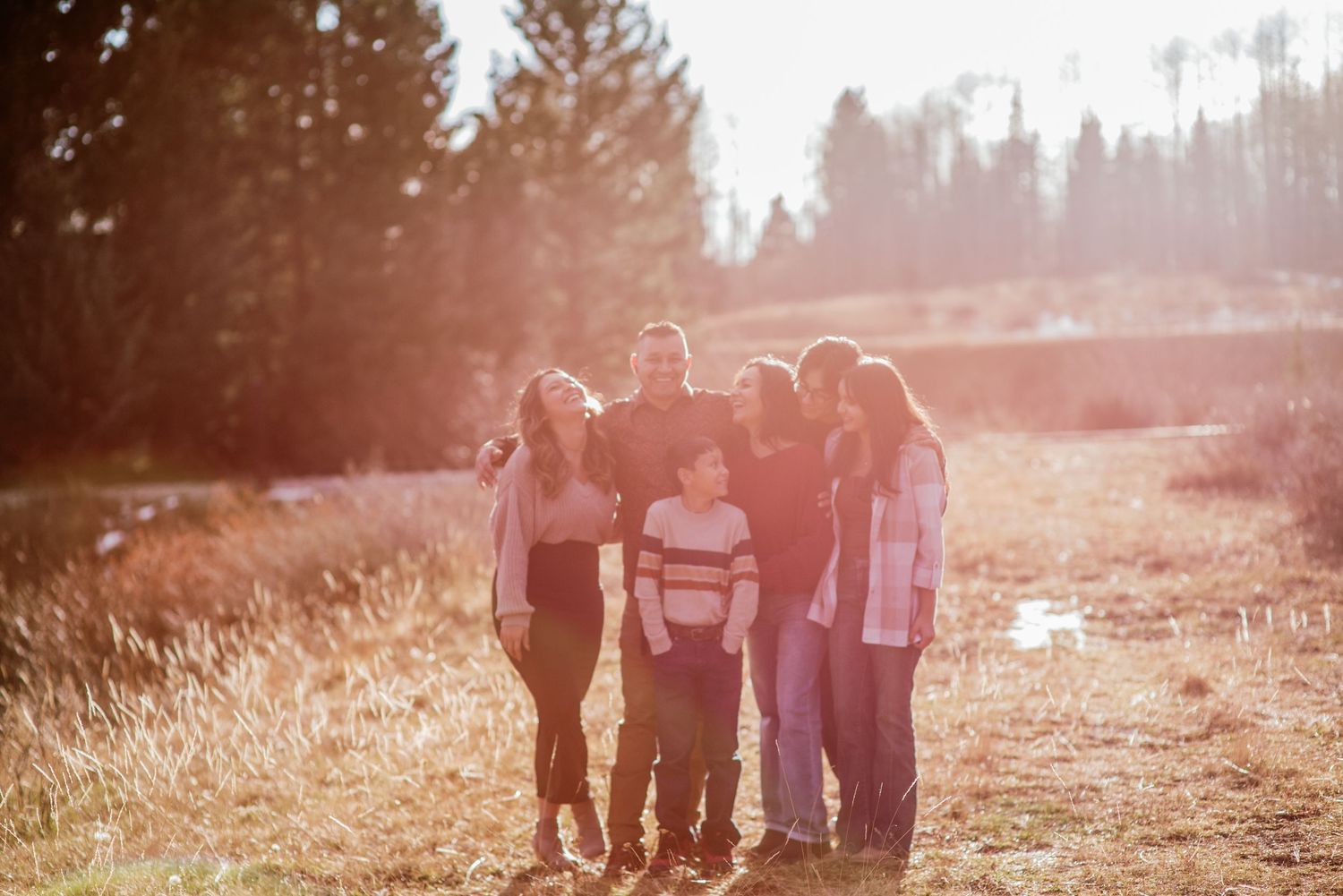 Group standing together on a sunlit trail in nature with warm golden light filtering through pine trees in the background.