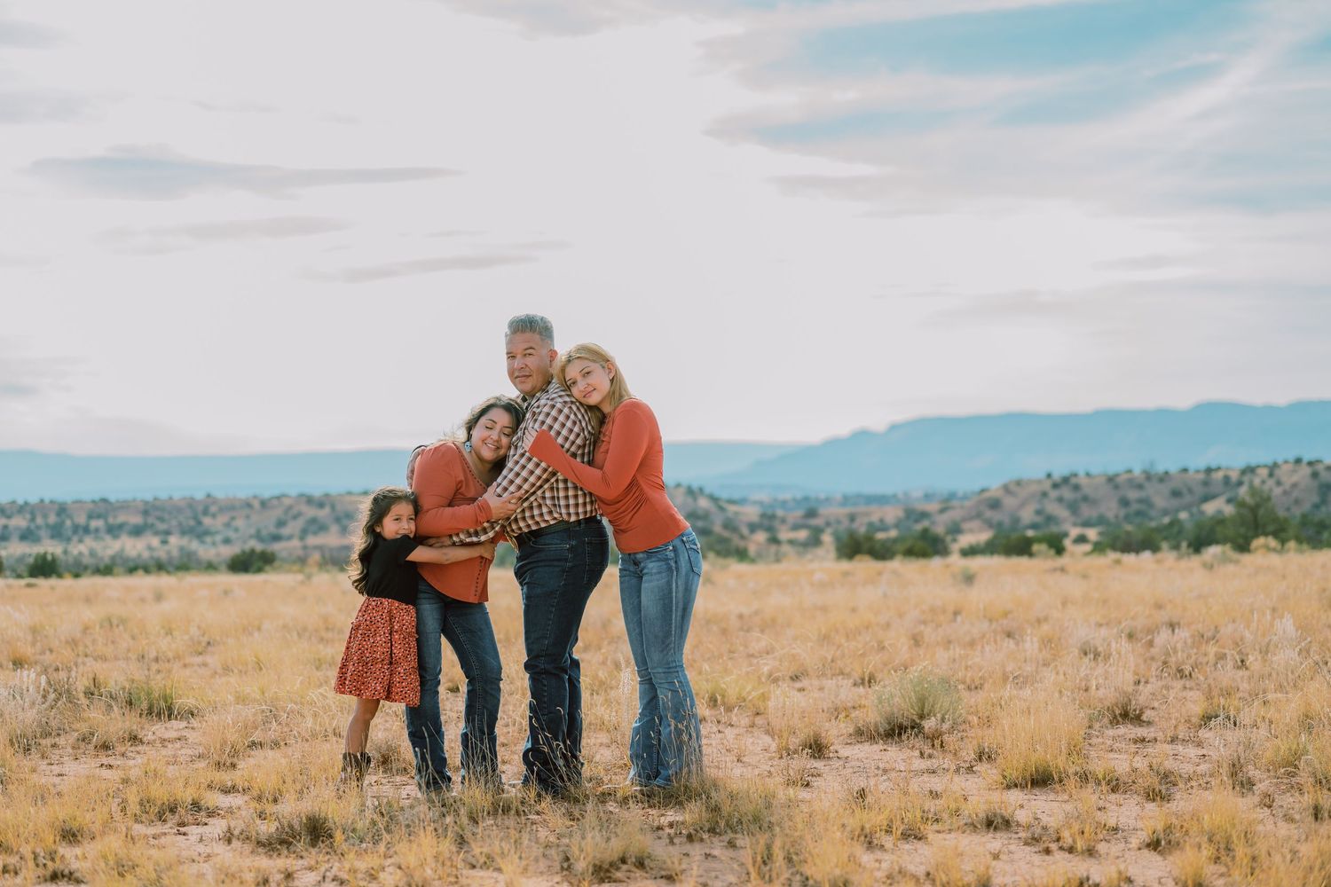 A family poses together in an open field with mountains and blue sky in the background during autumn.