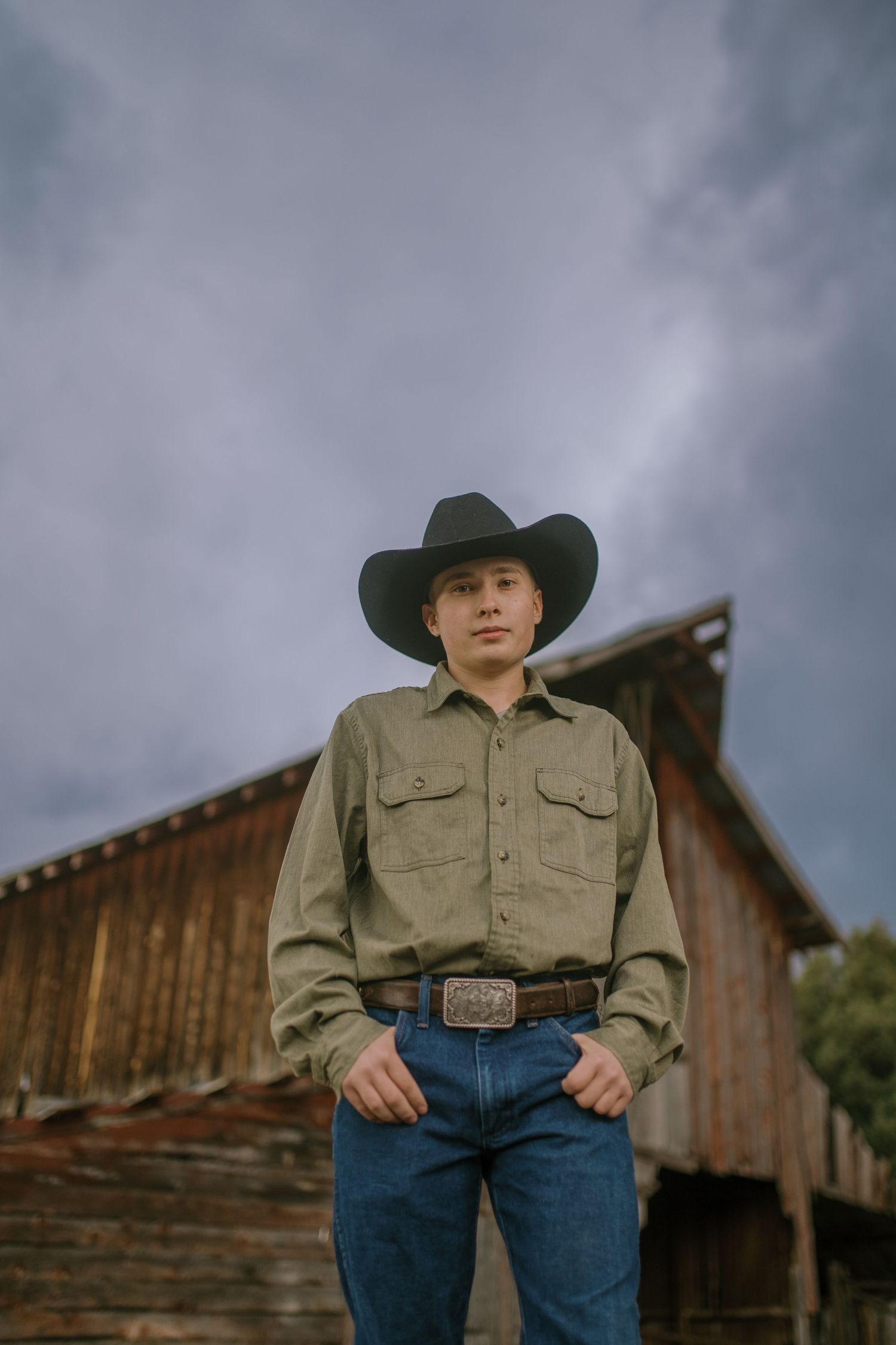 A rustic country scene with someone in a cowboy hat and denim standing in front of a weathered wooden barn.
