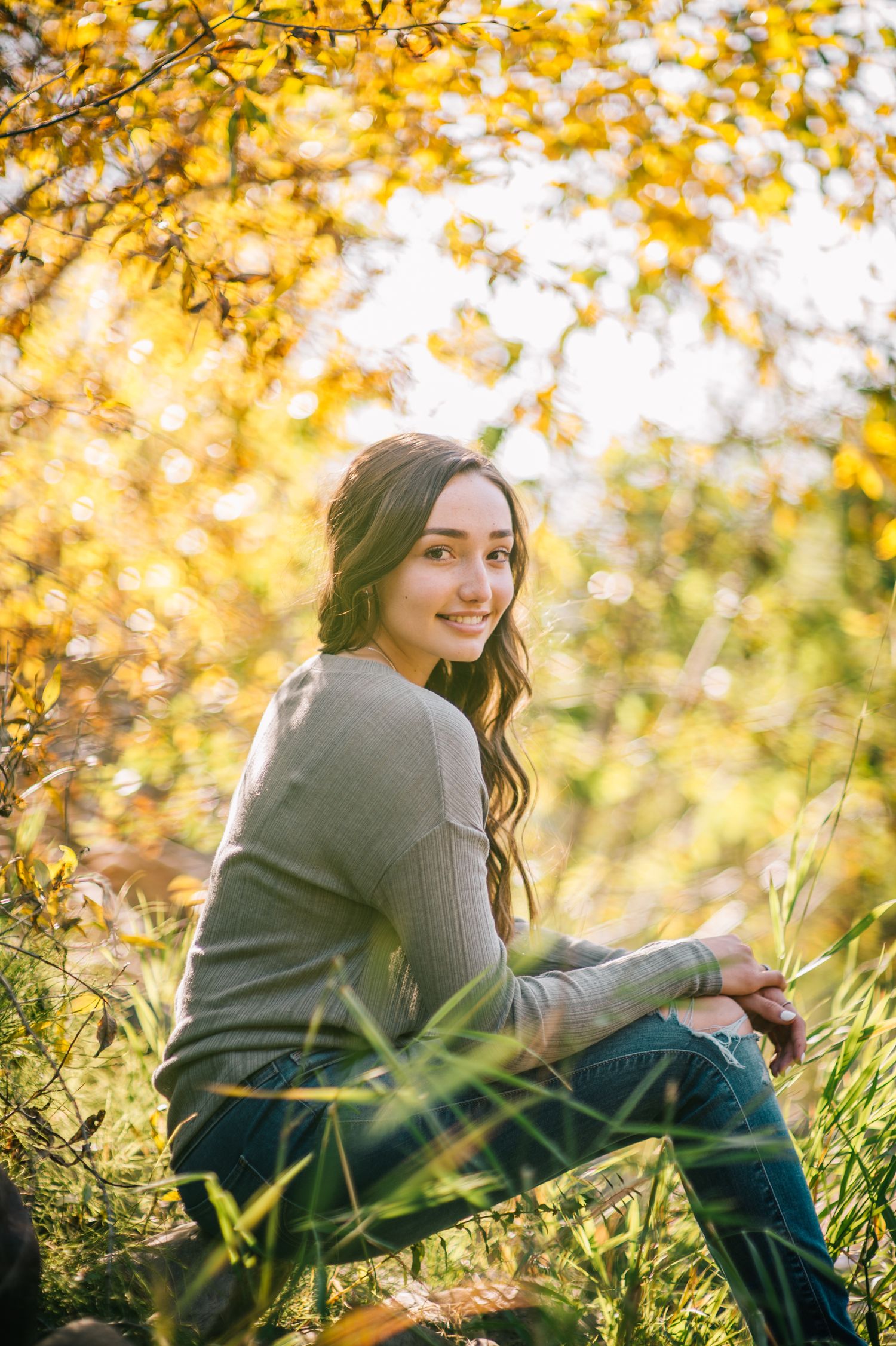Person in grey sweater relaxing in autumn grass with golden leaves overhead.