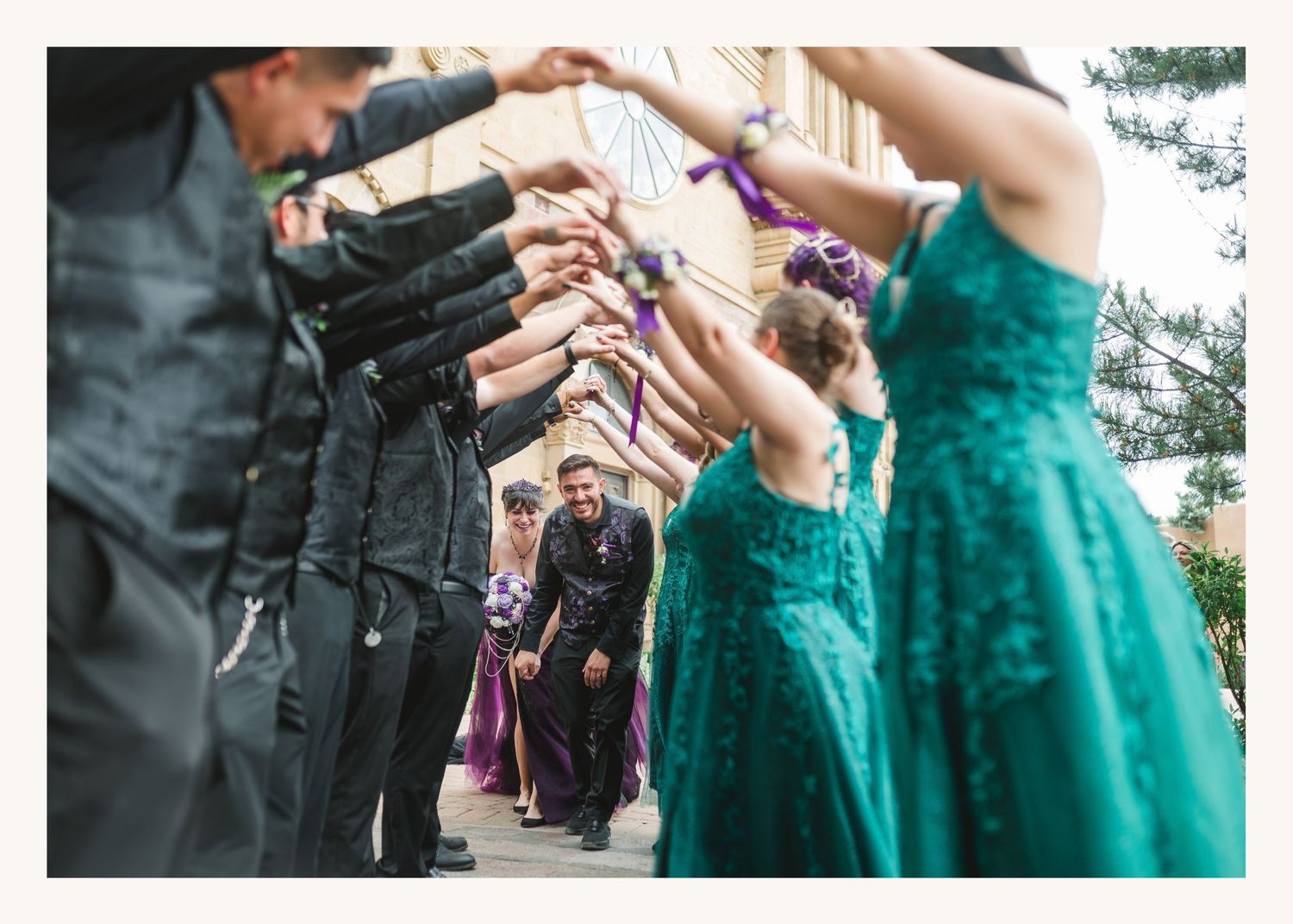 Wedding party forming an arch tunnel for newlyweds to walk through outdoors at a formal ceremony.