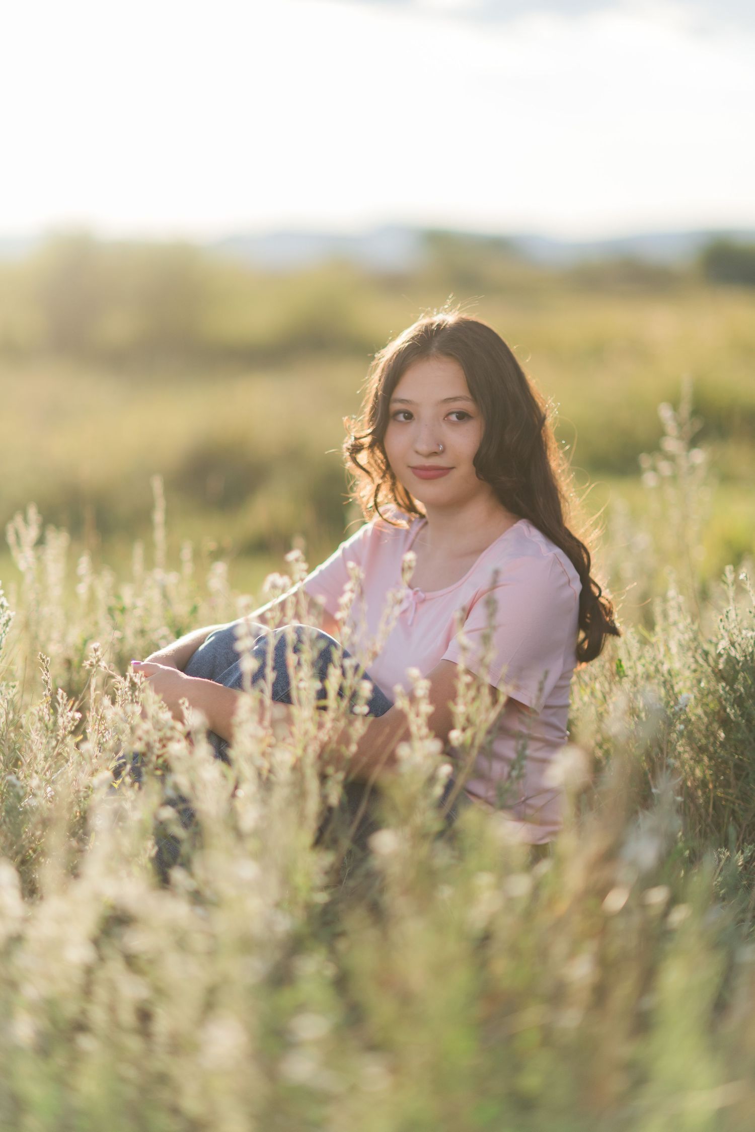 Young woman poses gracefully in a dreamy field of wildflowers at golden hour with soft natural lighting.
