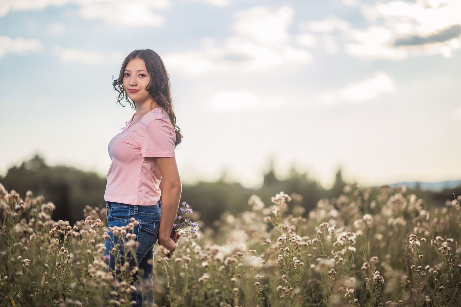 A person in a pink top stands thoughtfully in a serene wildflower field during golden hour.