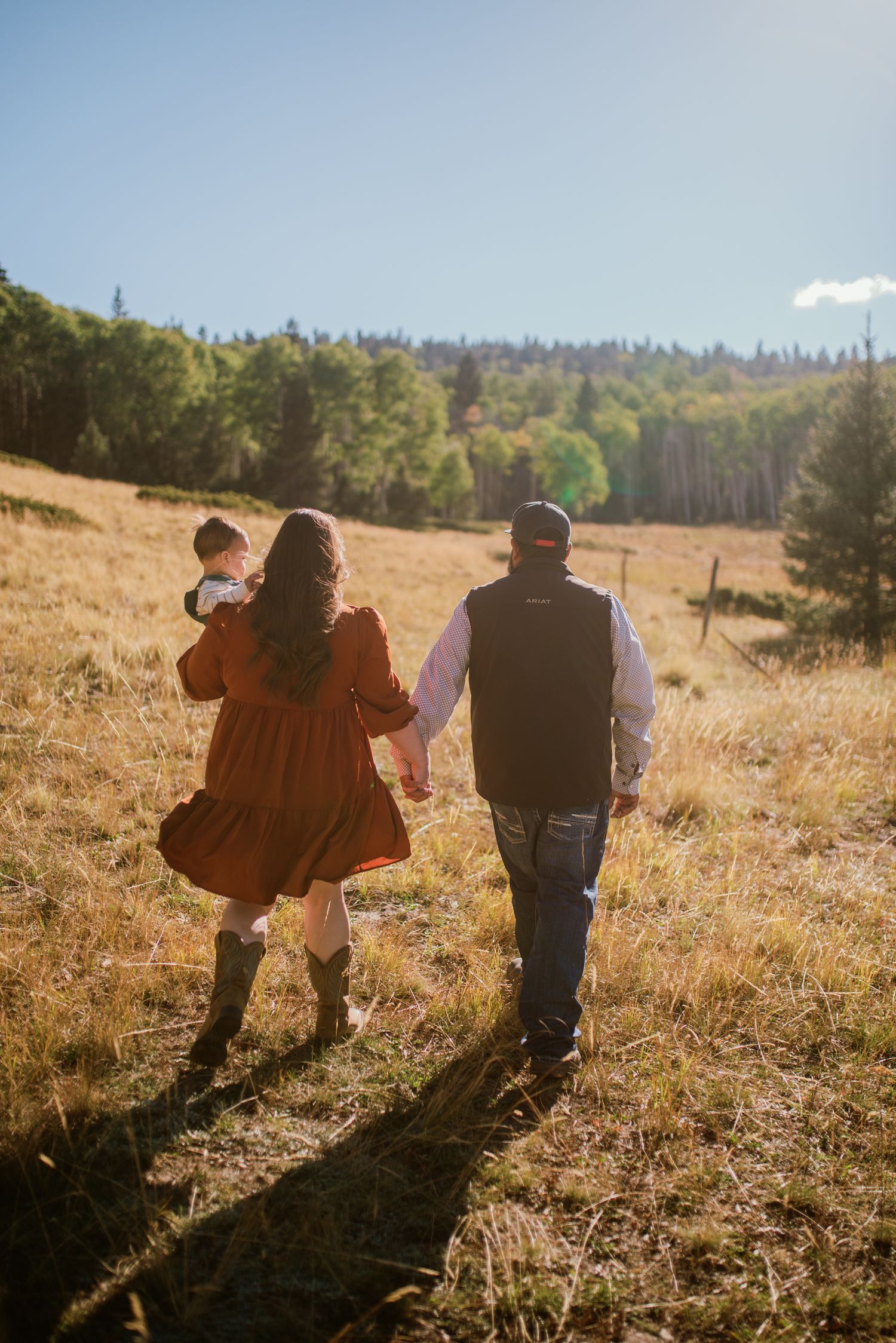 Family of three walking hand-in-hand through a sun-dappled forest trail near Santa Fe — tender moment by Quiet Light by The Amoras.