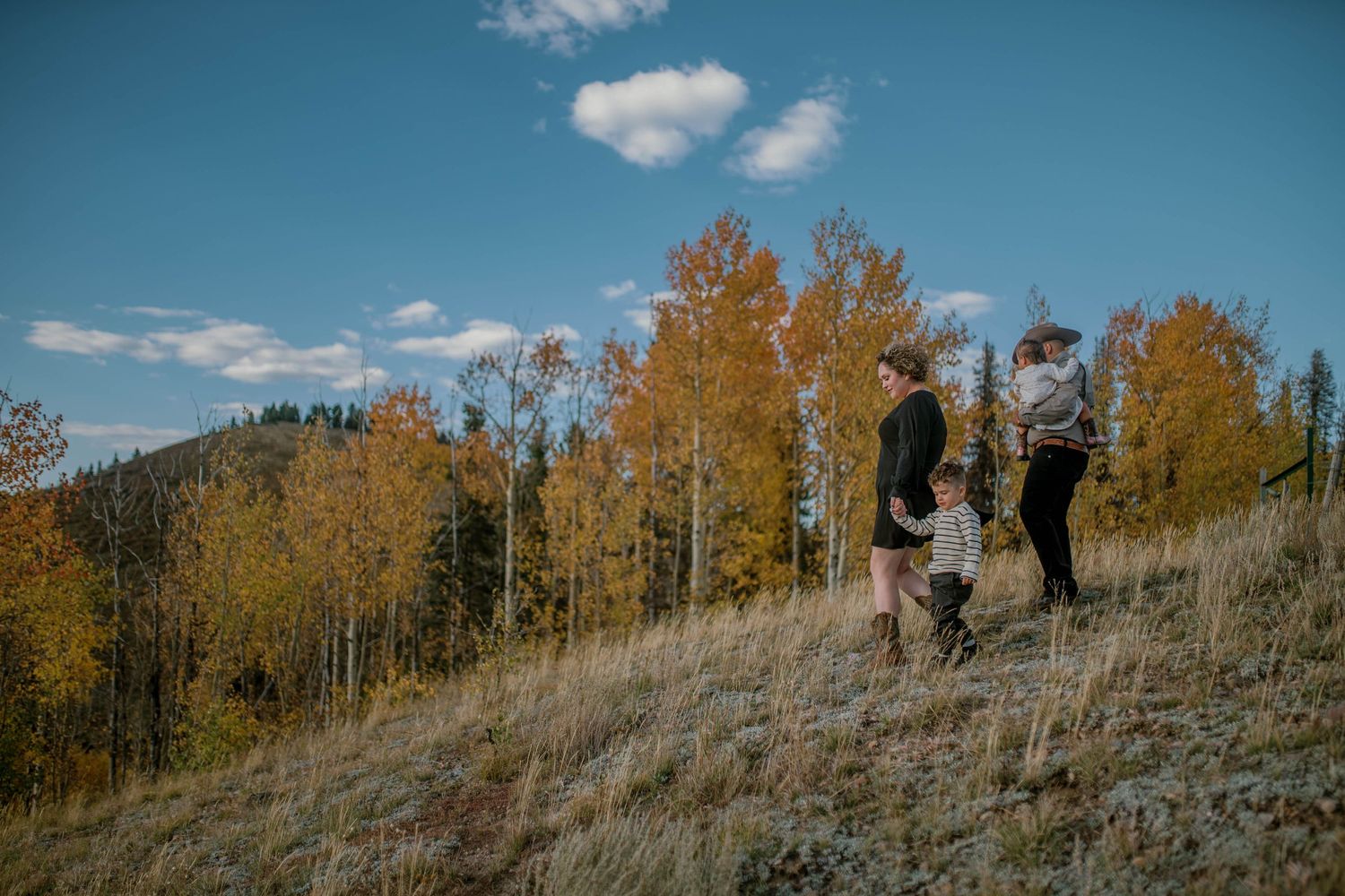Young family of four walking through autumn trees in northern New Mexico — warm, golden family session by Quiet Light by The Amoras.