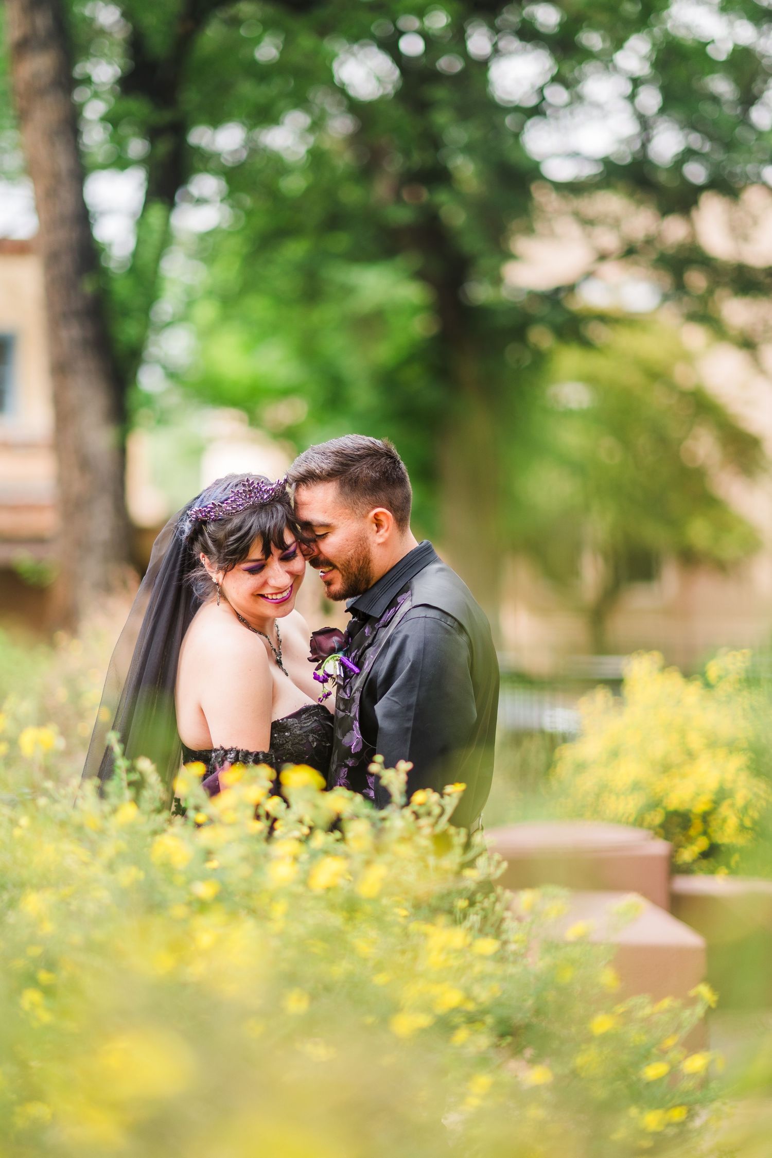 A bride and groom share a romantic moment surrounded by yellow wildflowers in a lush garden setting.