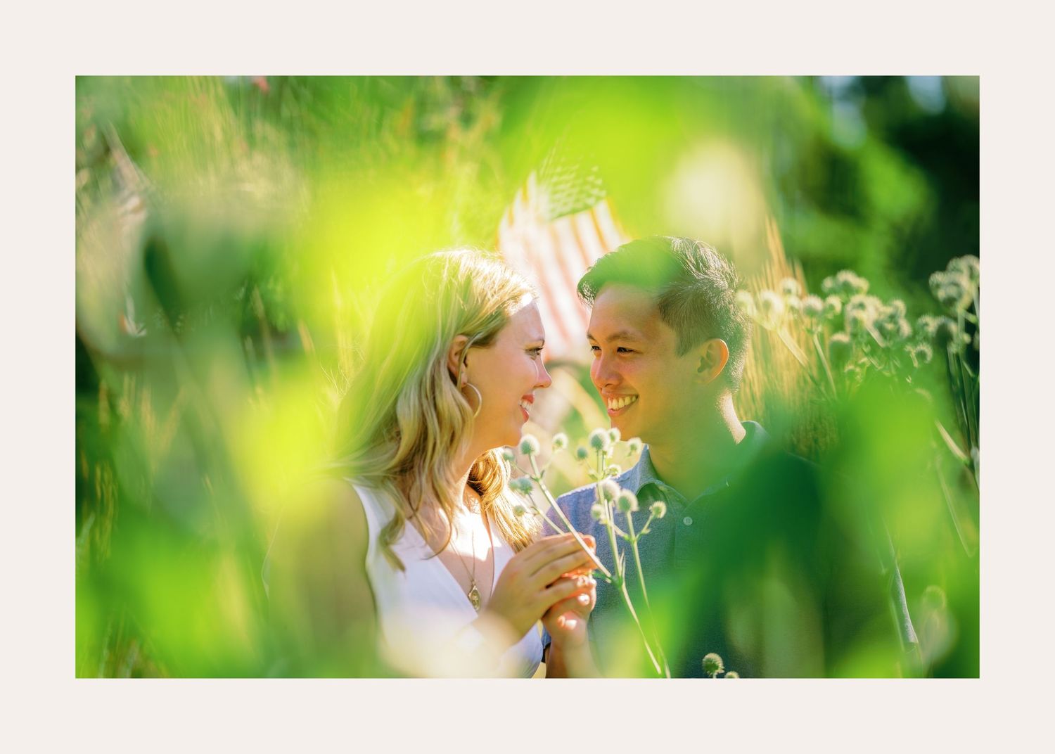Romantic couple shares tender moment among wildflowers in soft sunlit meadow with dreamy green bokeh background.