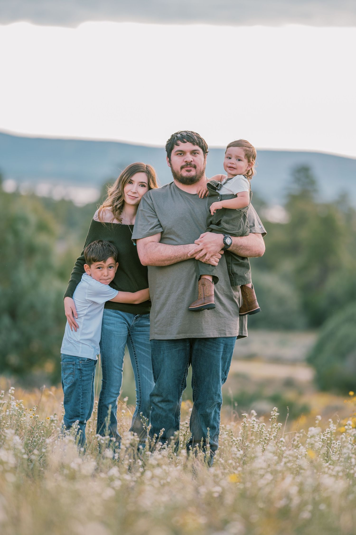 Family posing together in meadow of yellow wildflowers with mountains in background.