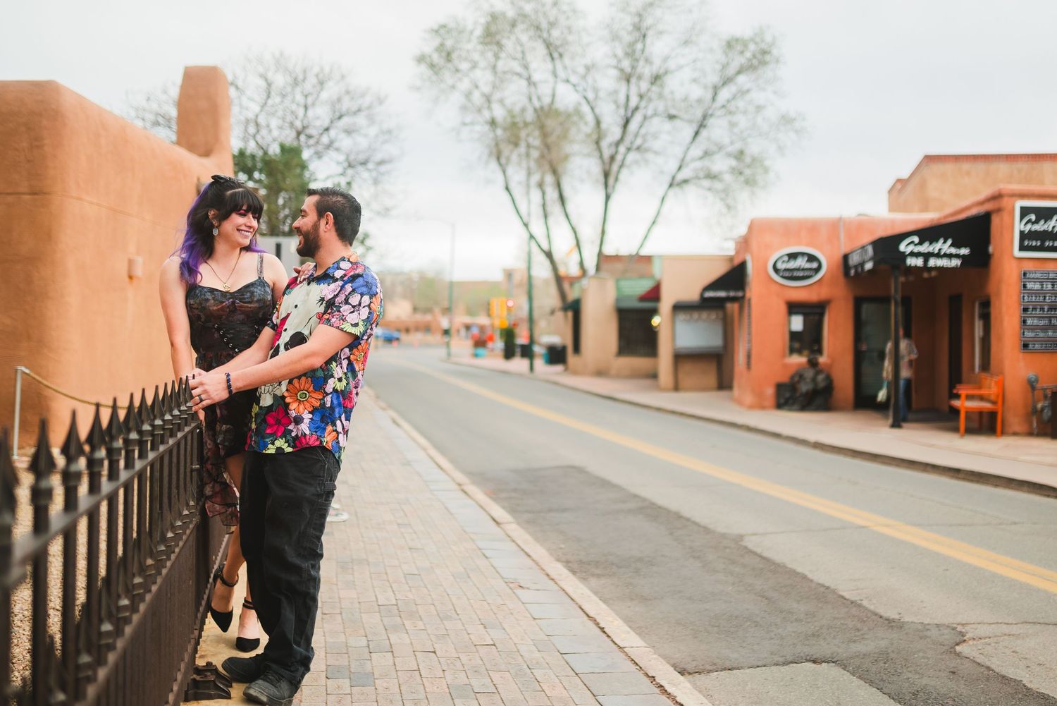 Couple sharing a romantic moment on a colorful small-town street, woman in black dress, man in floral shirt.