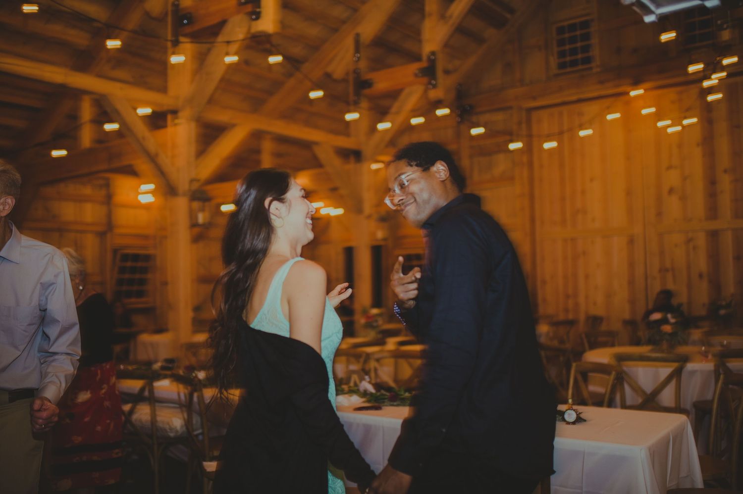 Wedding celebration inside a warmly lit timber frame barn with exposed beams.