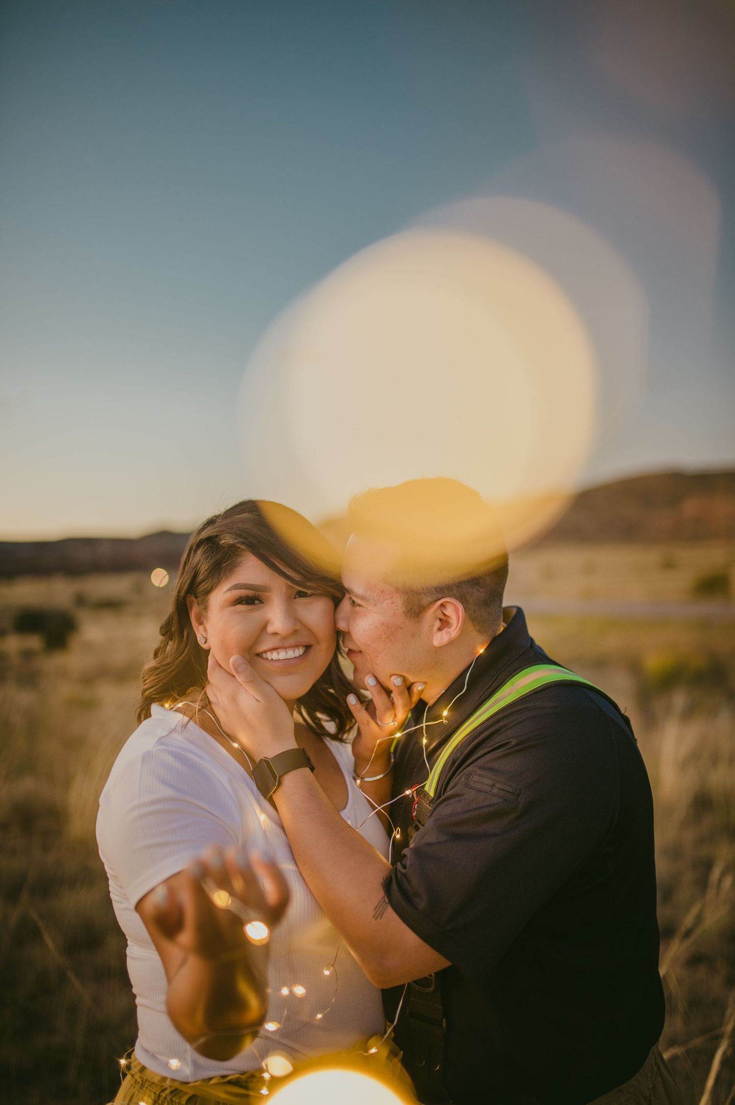 A couple laughs together during their sunset engagement session with dreamy bokeh lights.