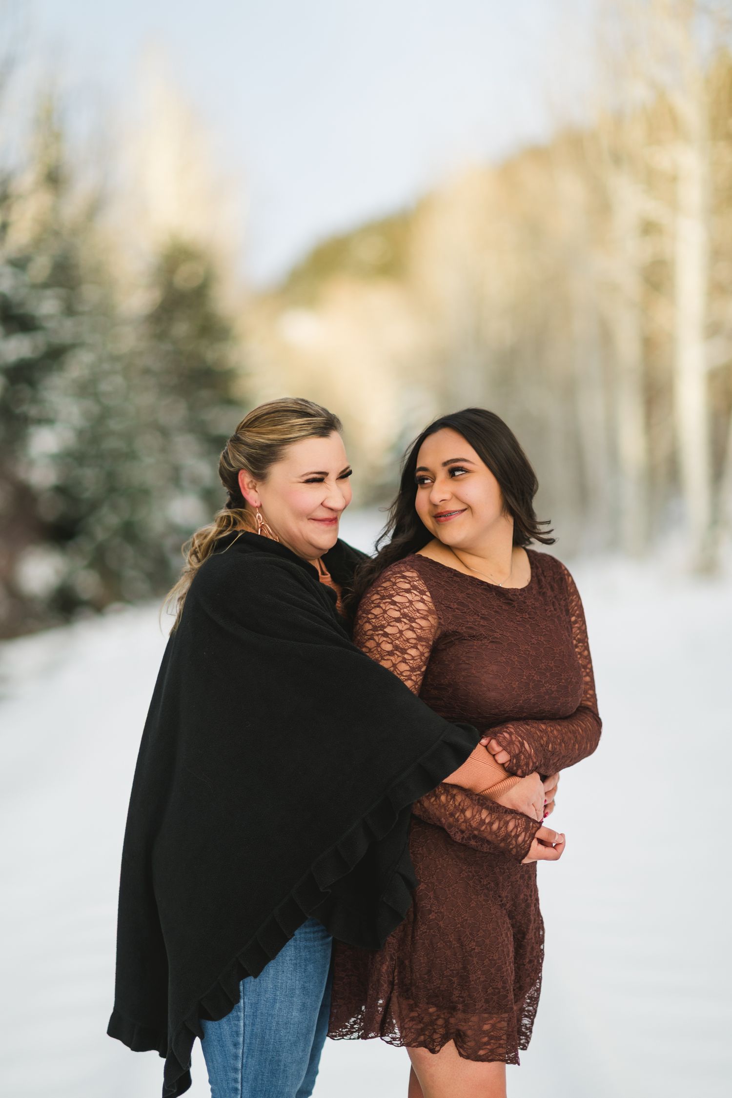A couple shares a tender moment together in a snowy winter landscape with trees in the background.