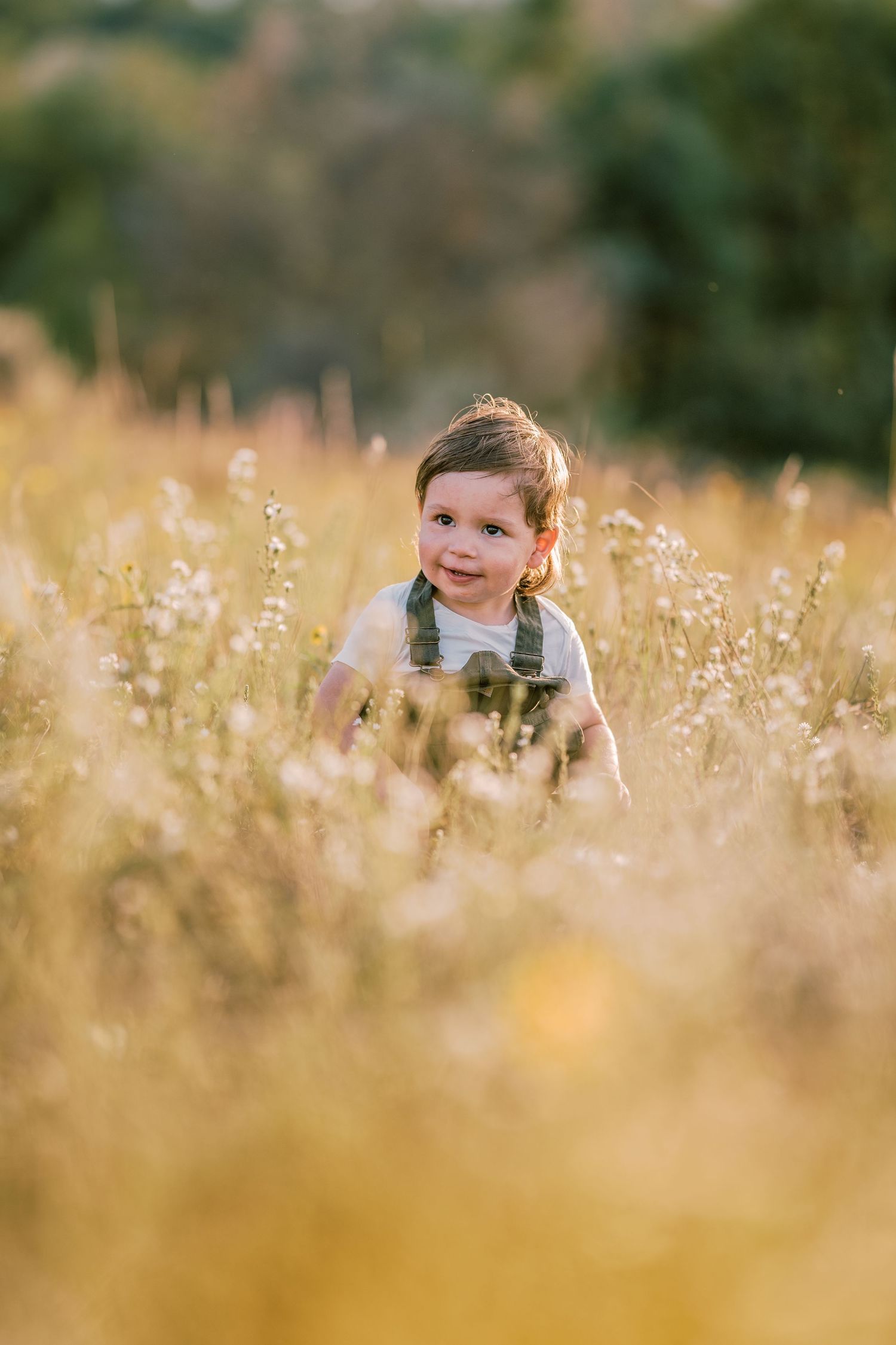 Child's smiling face emerging from a field of yellow wildflowers during golden hour.