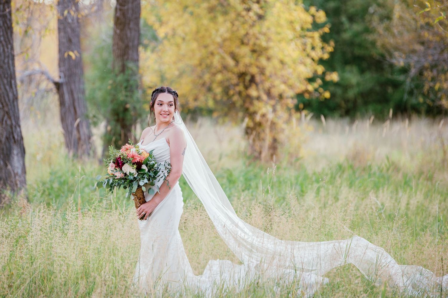 Fall bride in a grassy field with soft autumn trees behind her — outdoor portrait by The Amoras in northern New Mexico.
