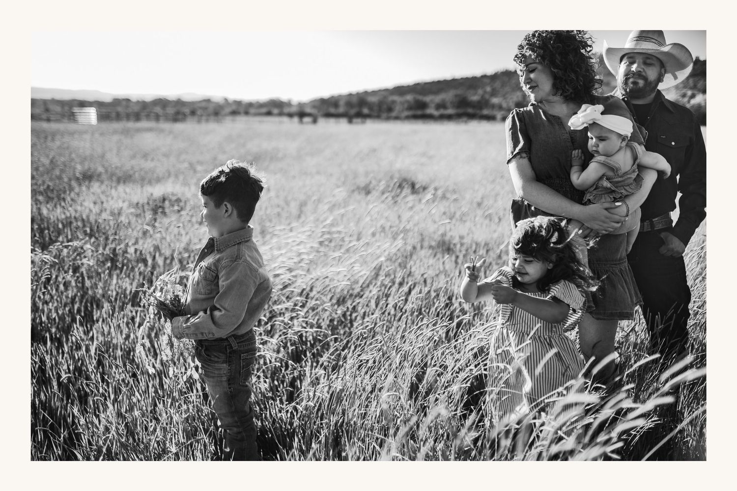 Black and white photo of a family with children standing in a tall grass field in a rural landscape.