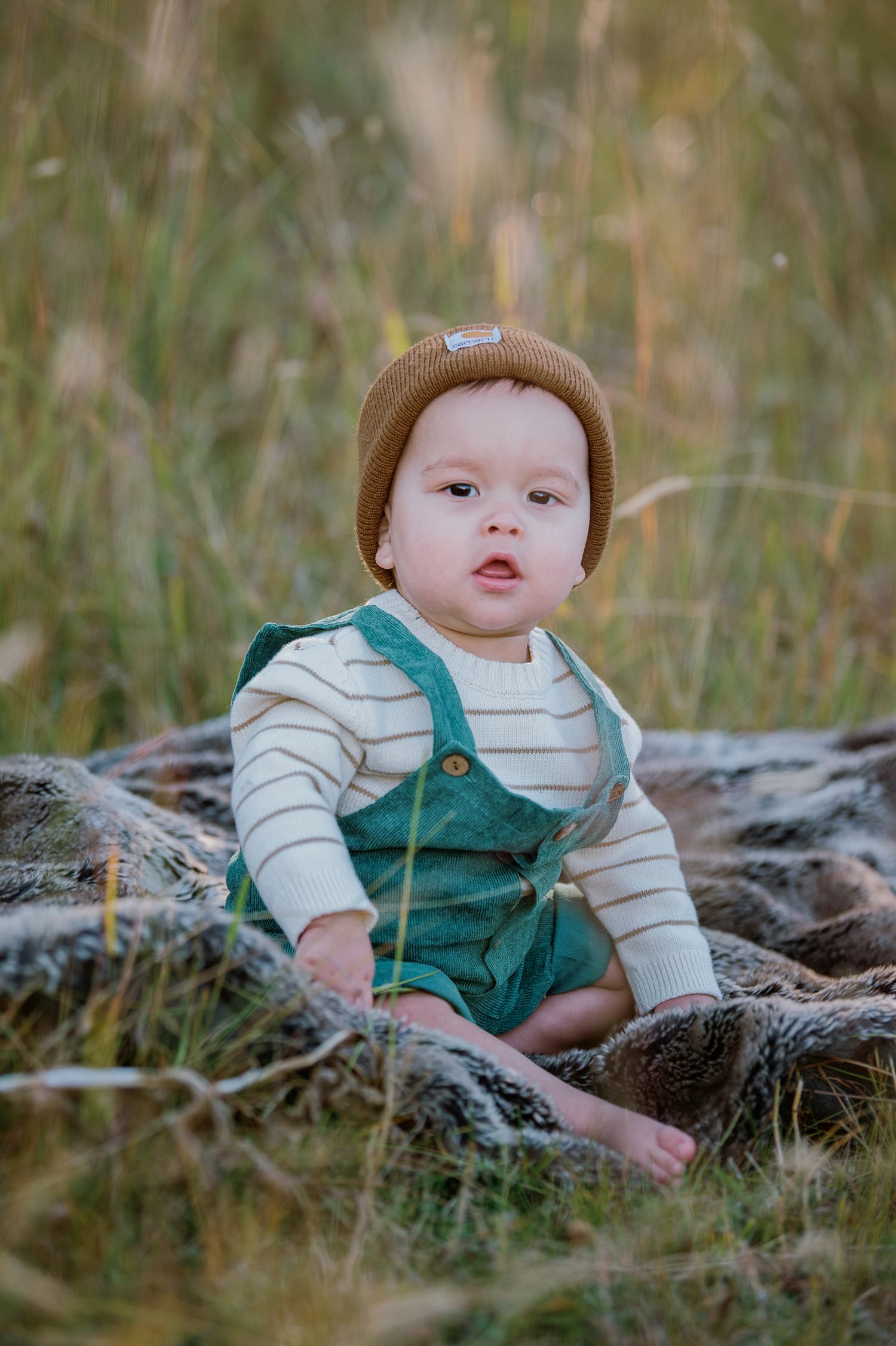Small figure in green overalls on rustic wooden log surrounded by tall grass.