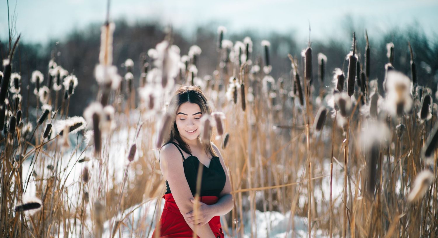 Portrait of person in red dress among tall winter cattails.