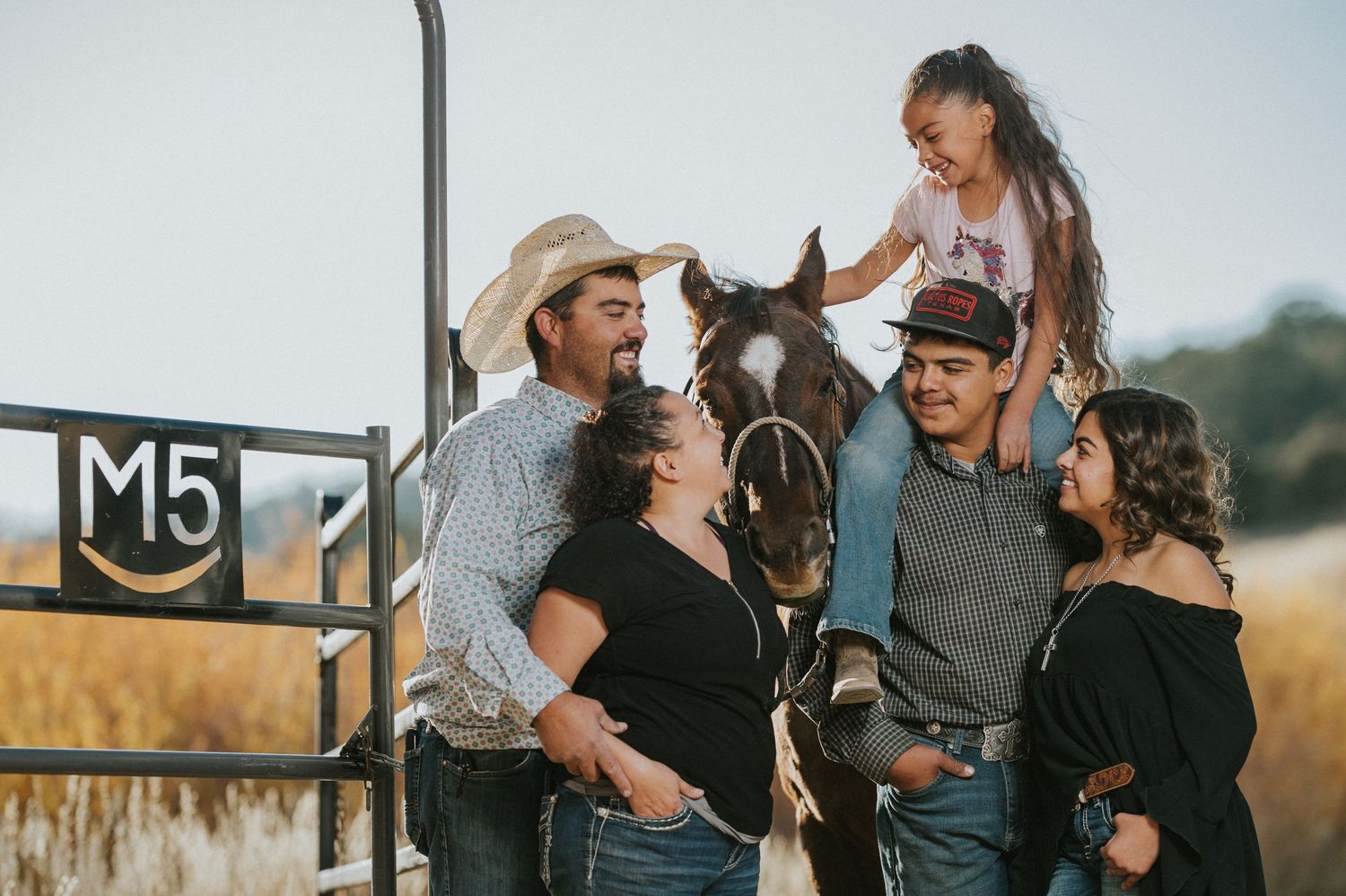 A family poses together affectionately in a golden field at sunset.