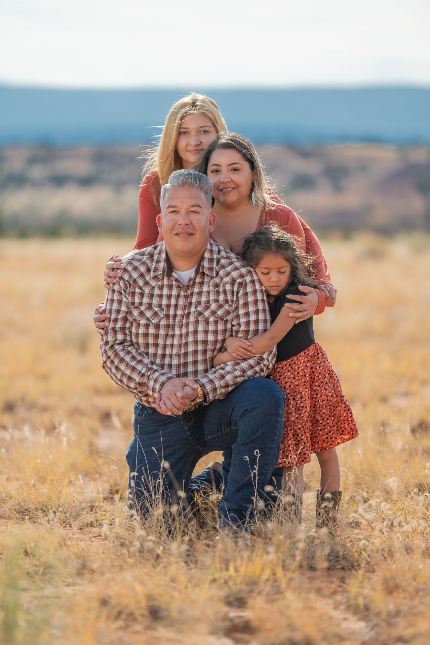 Parents with teenage and young daughters in a serene Abiquiú desert field — captured in soft, golden light by The Amoras.