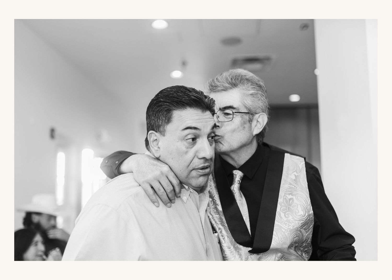 Two men share an emotional embrace in a black and white candid photo at a formal event.