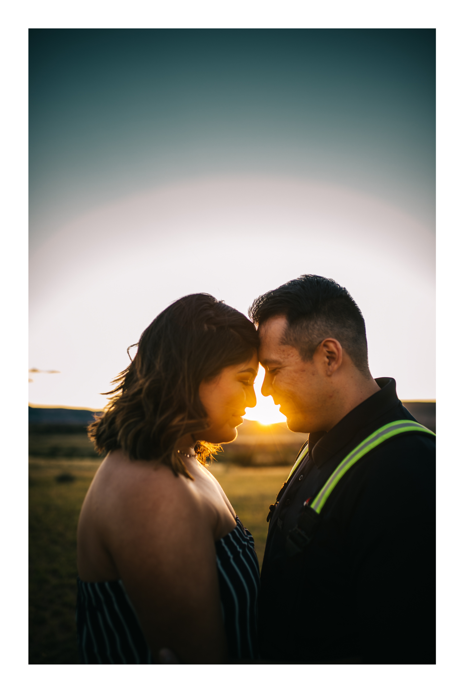 Couple sharing an intimate moment forehead-to-forehead at golden sunset in an open field.
