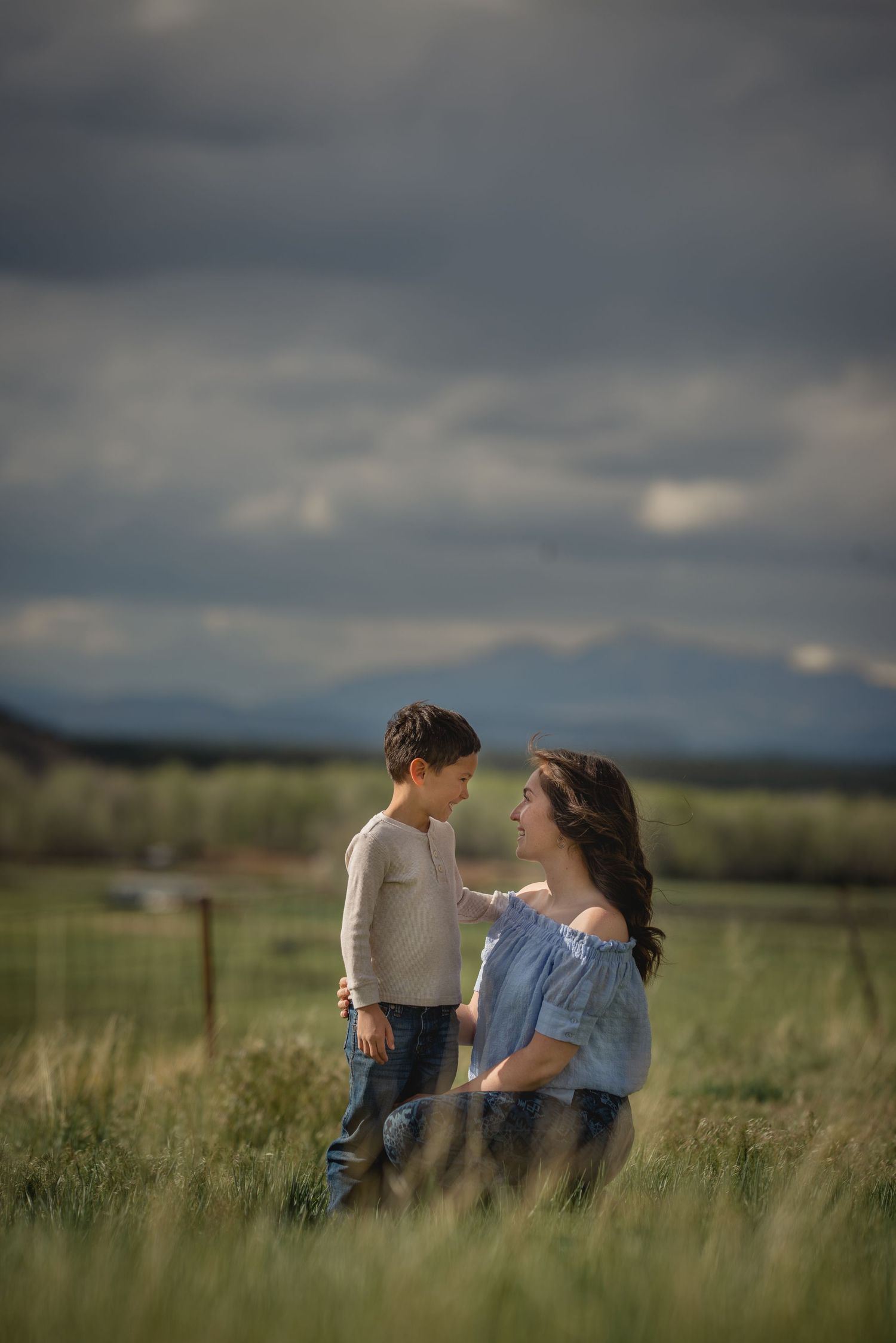 A tender moment captured in a green field with mountains and moody clouds in the background.