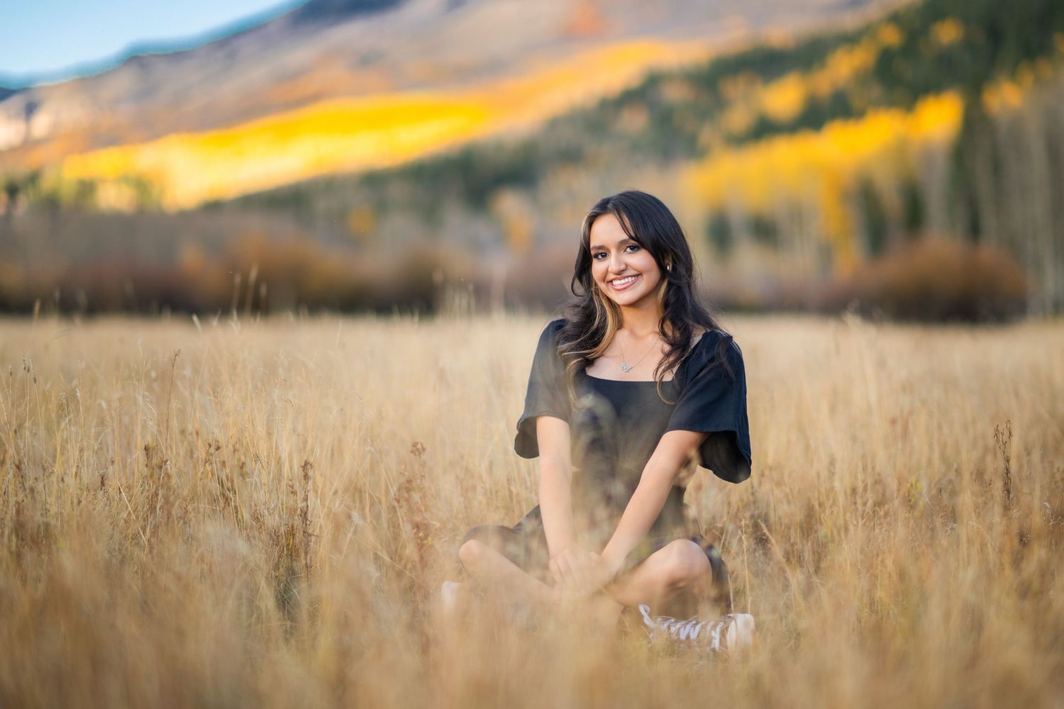A woman in a black top poses gracefully in a golden autumn wheat field at sunset.