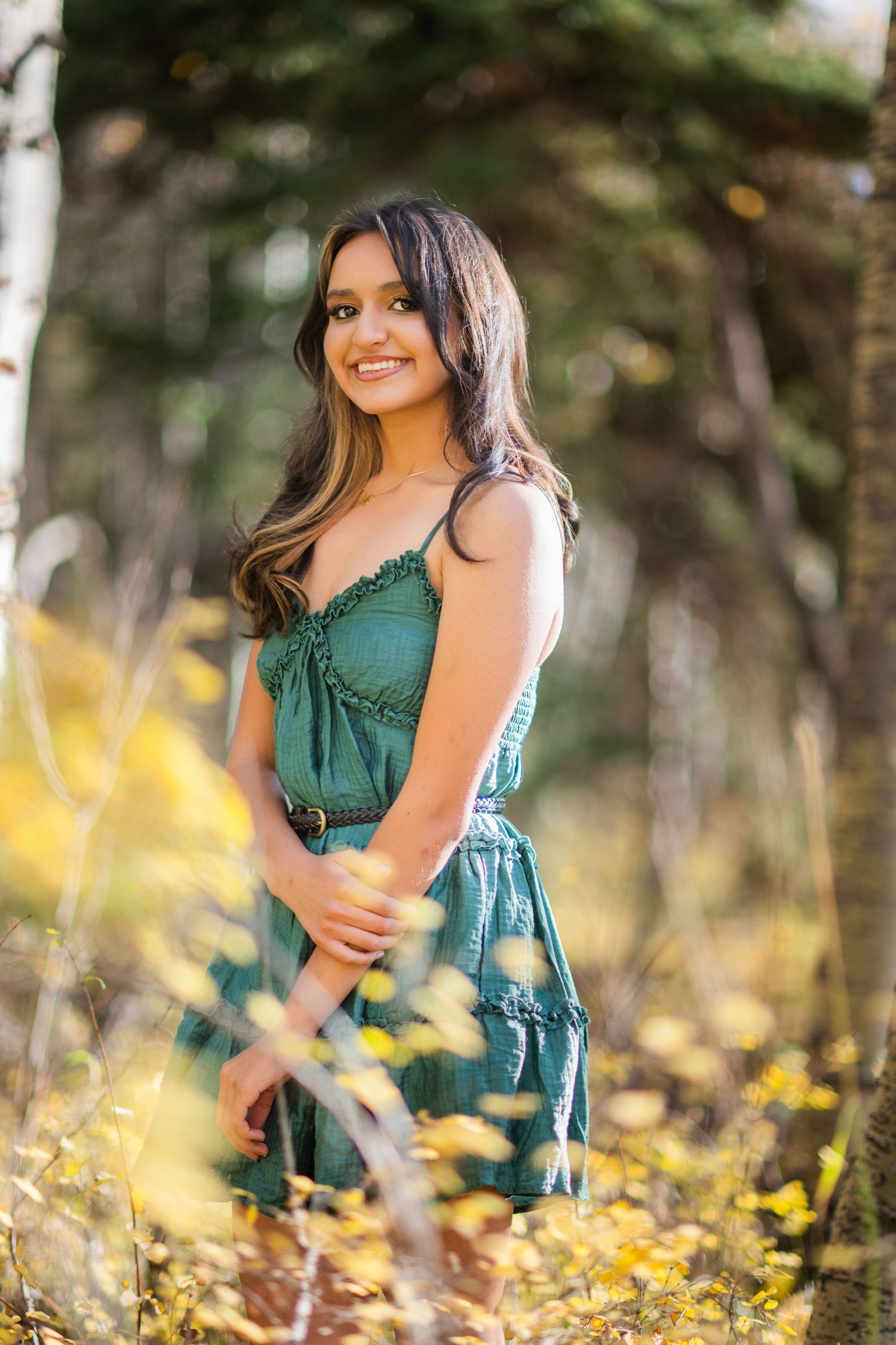 A woman in a green dress poses outdoors among autumn foliage in a series of candid portrait shots.